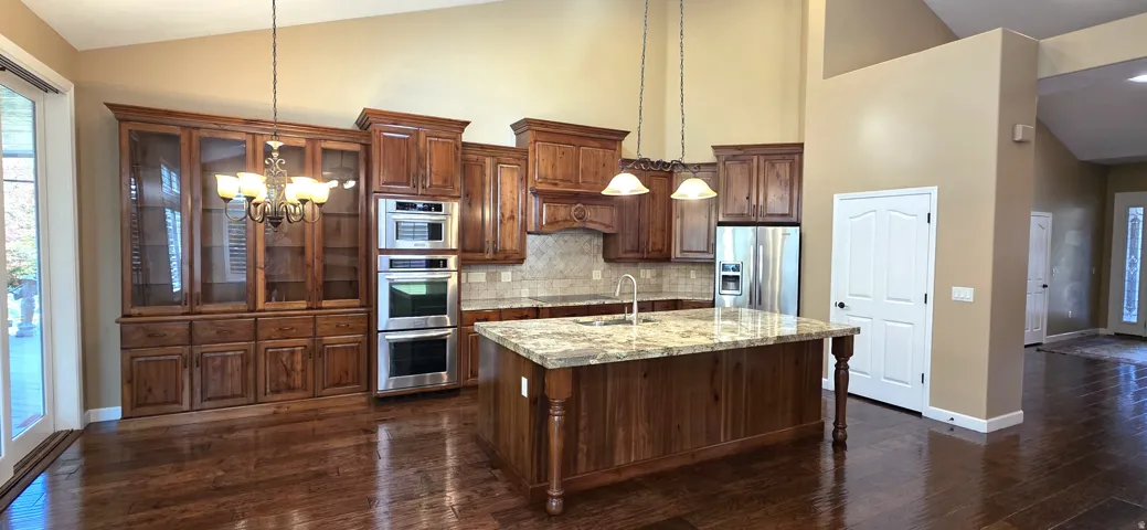 Kitchen featuring wood-finish cabinetry, a large center island with a stone countertop, stainless steel double ovens, and wood-finish flooring