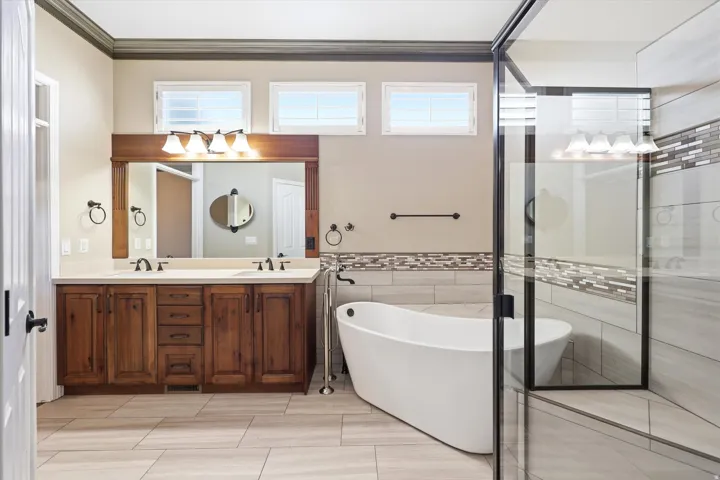 Spacious bathroom featuring a double vanity with wood cabinetry, a large frameless mirror, and a standalone soaking tub
