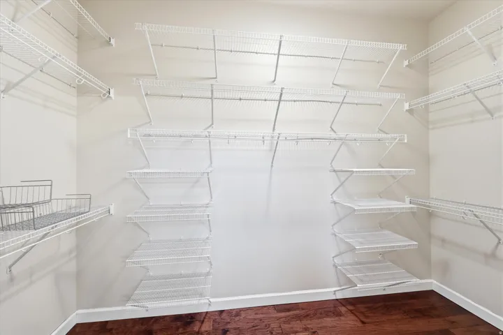 Walk-in closet featuring extensive wire shelving, multiple hanging rods, corner shelving units, wood-finish flooring, and white baseboards
