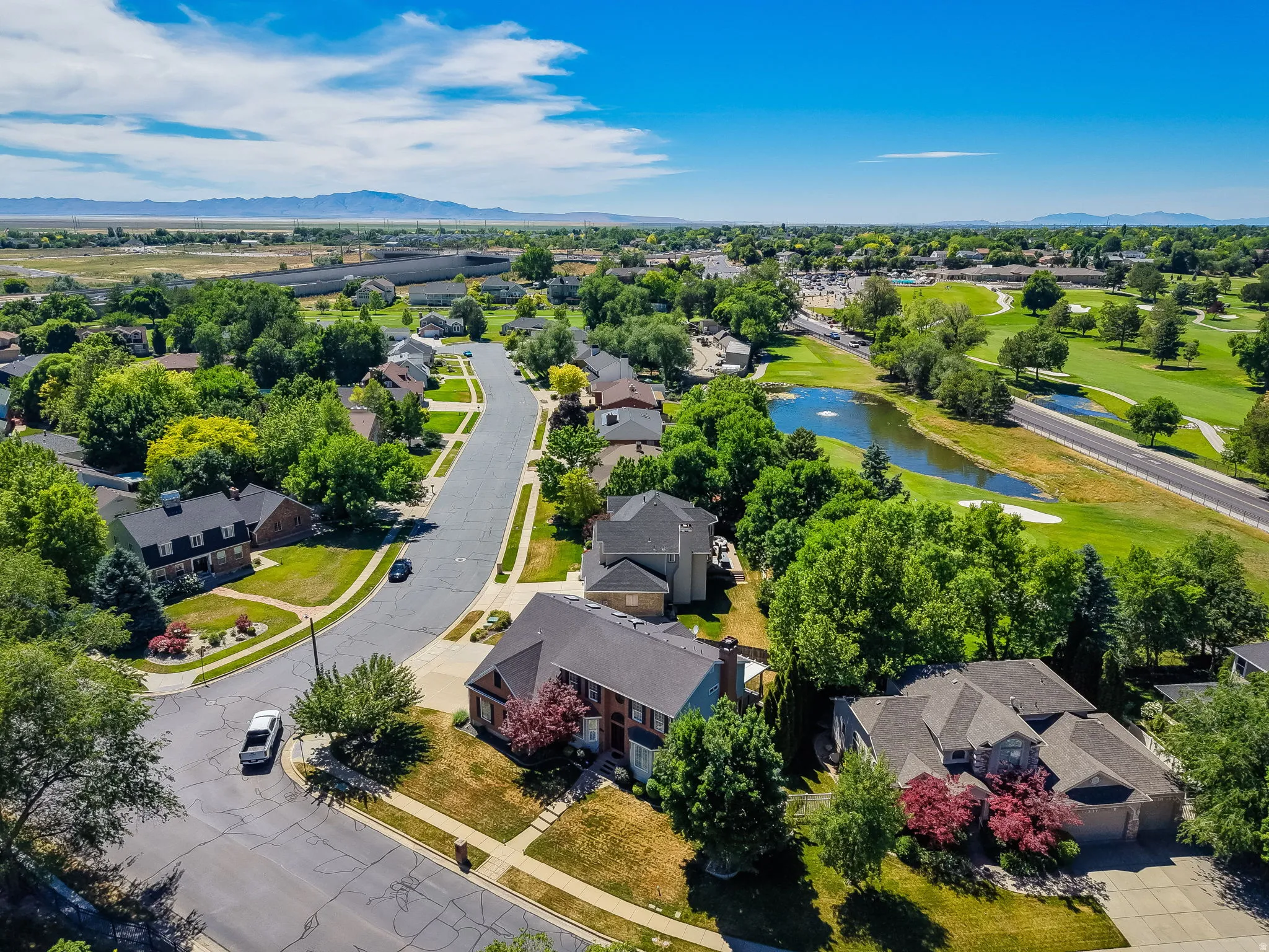 Expansive community featuring mature trees, a golf course with a water feature, and mountain scenery in the distance