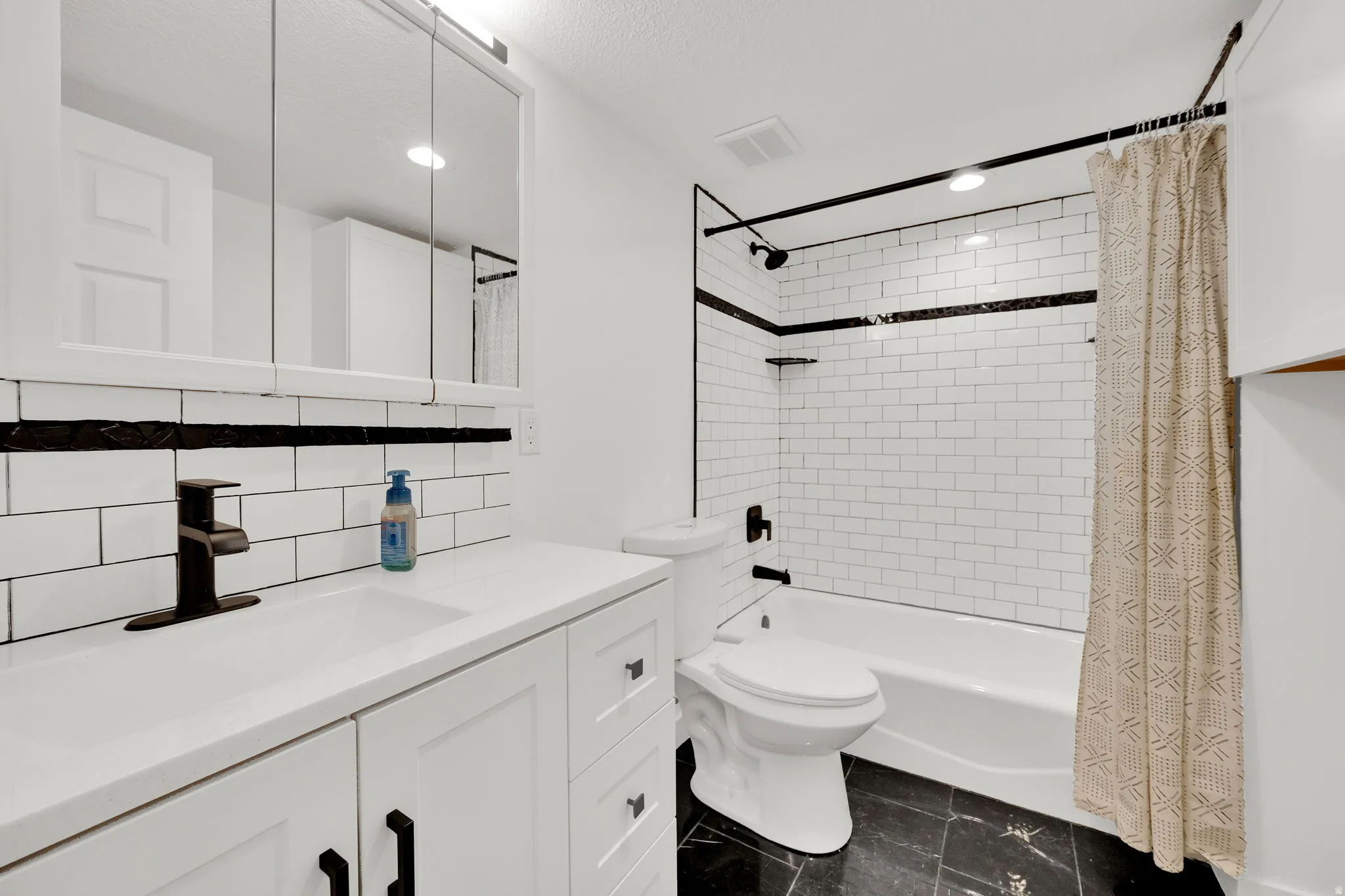 Bathroom featuring a white subway tile surround with a dark accent band, dark floor tiling, white vanity with integrated sink, dark faucet, and a wall-mounted medicine cabinet