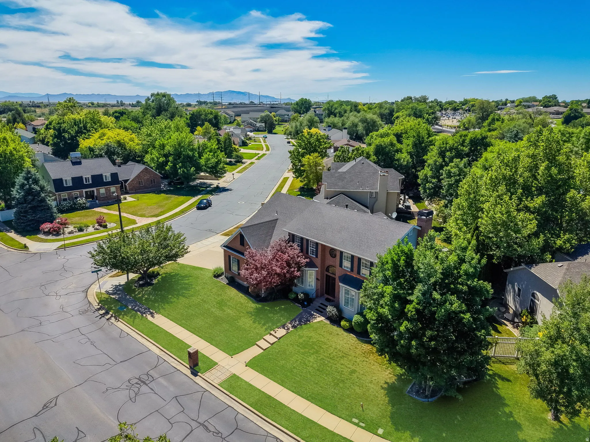 Brick residence featuring a gabled roof, mature landscaping, manicured lawn, and paved sidewalks