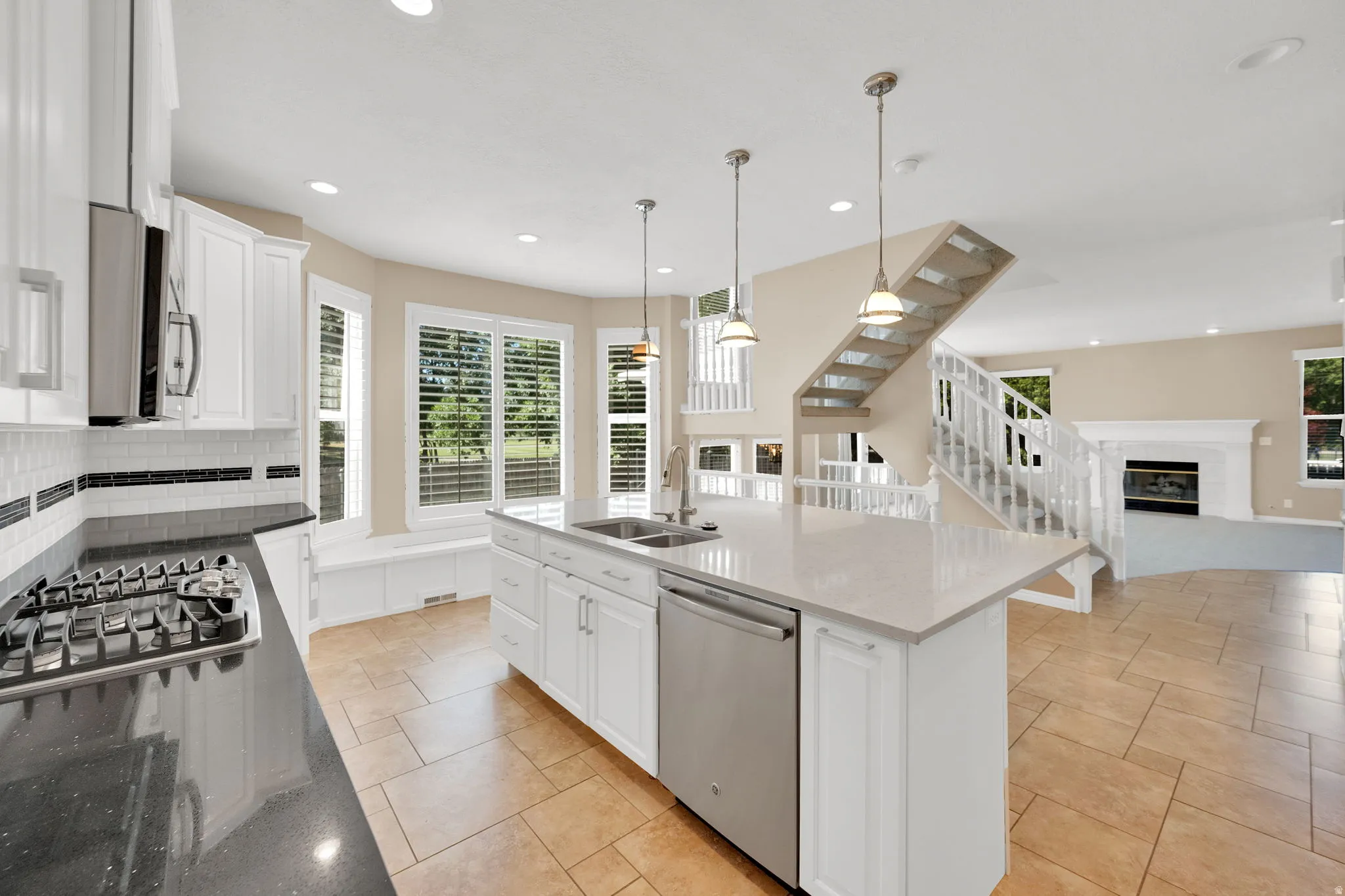 Open-concept kitchen featuring white cabinetry, a Quartz island with pendant lighting, a stainless-steel dishwasher, and a gas cooktop