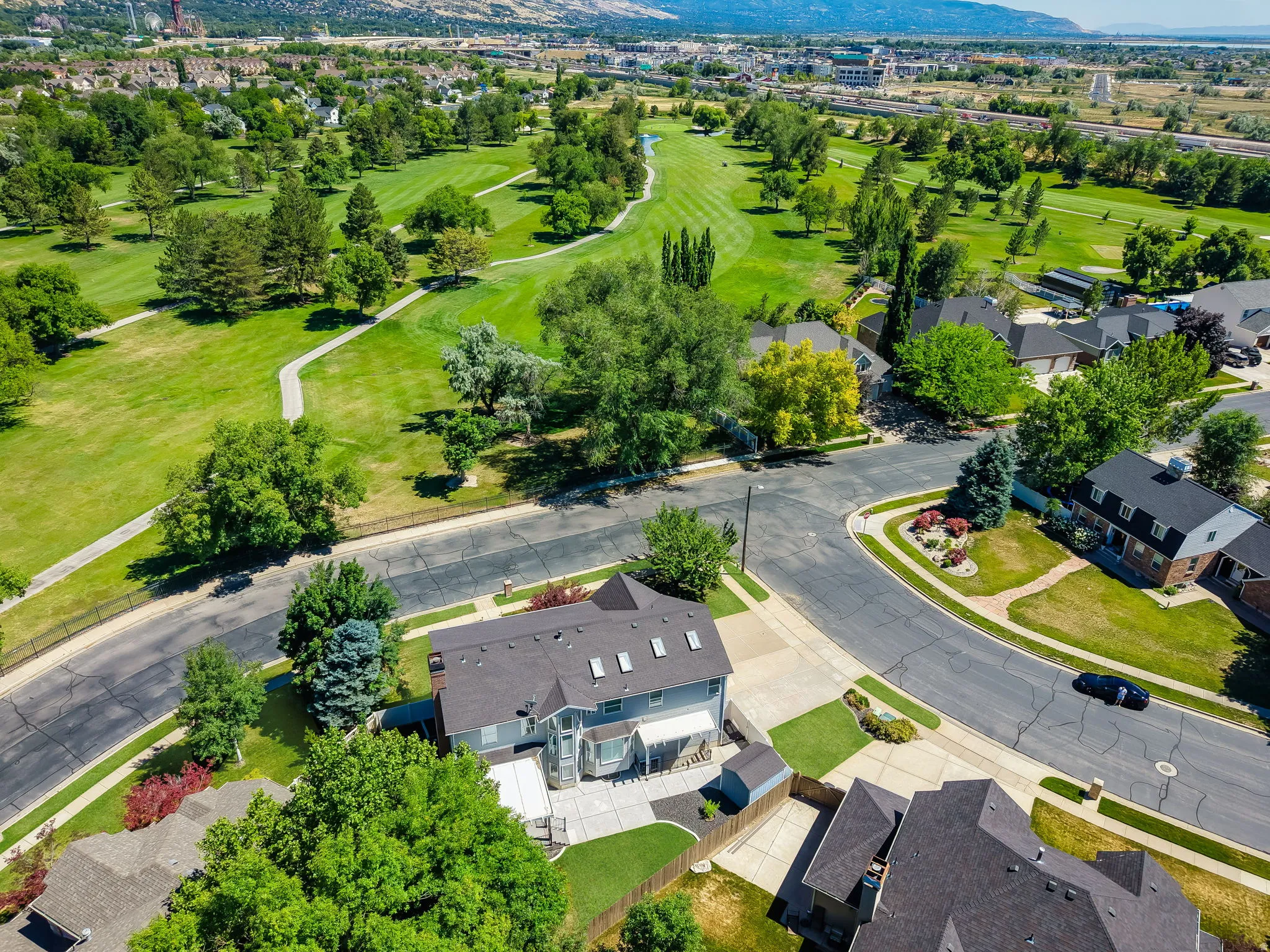 Expansive green space bordering the property, with a paved pathway, mature trees, and mountain scenery in the distance