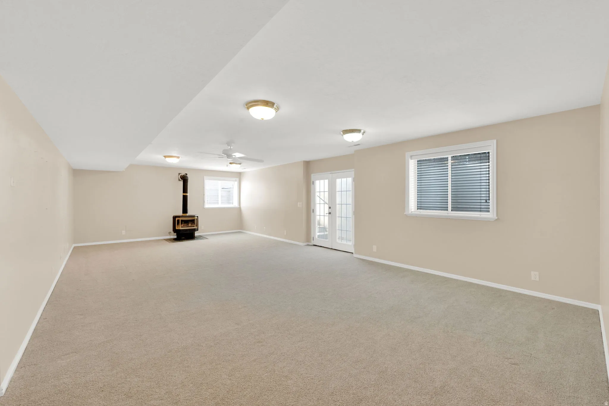 Spacious Great room featuring neutral carpeting, light beige walls, a gas stove, white trim, and a ceiling fan