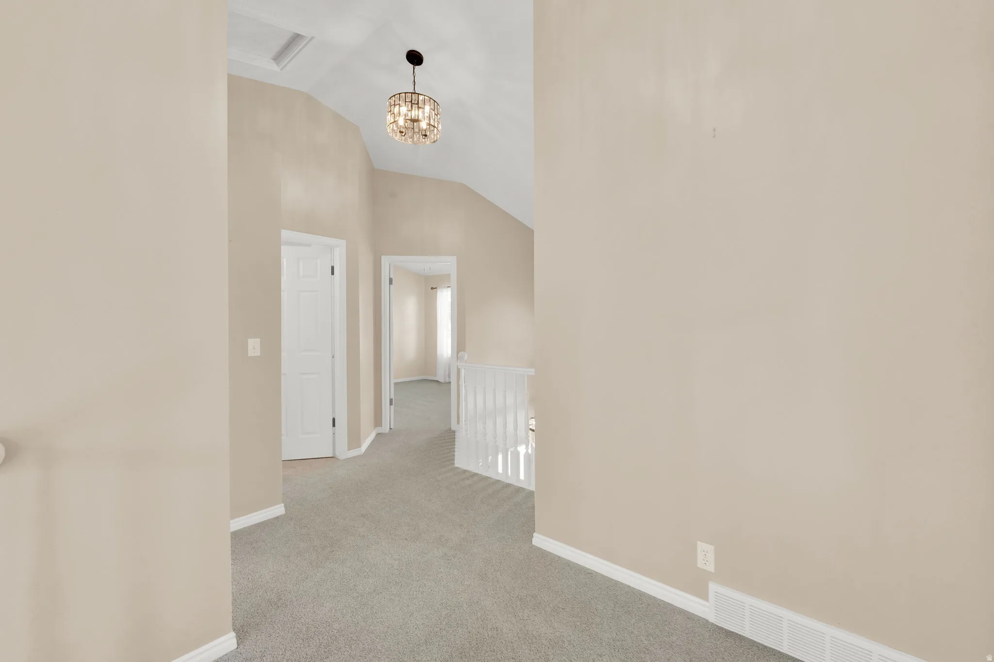 Carpeted hallway featuring a decorative chandelier, white trim, and doors