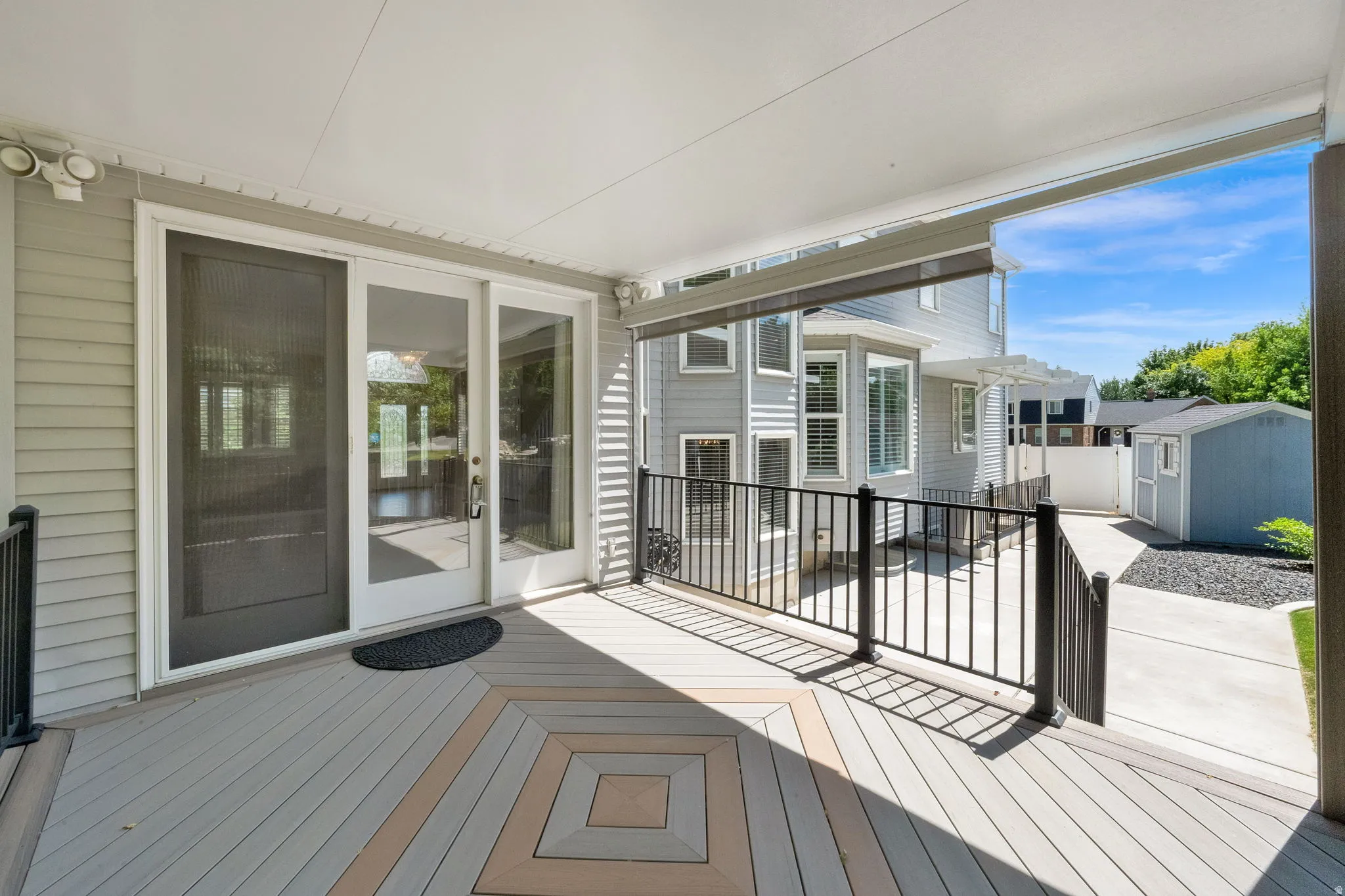 Covered outdoor deck featuring a decorative pattern in the flooring, black metal railings, and a sliding glass door for interior access
