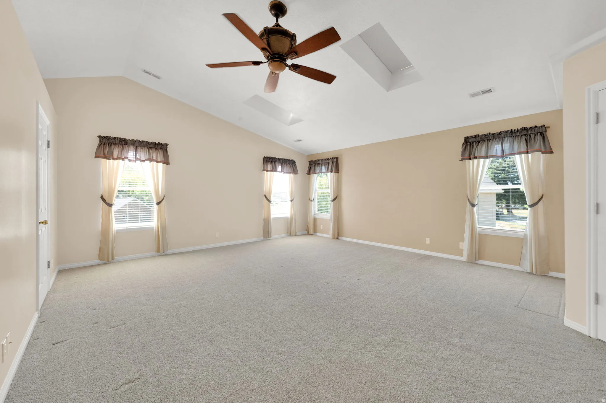 Spacious room featuring vaulted ceilings, a ceiling fan, two skylights, and multiple windows with blinds
