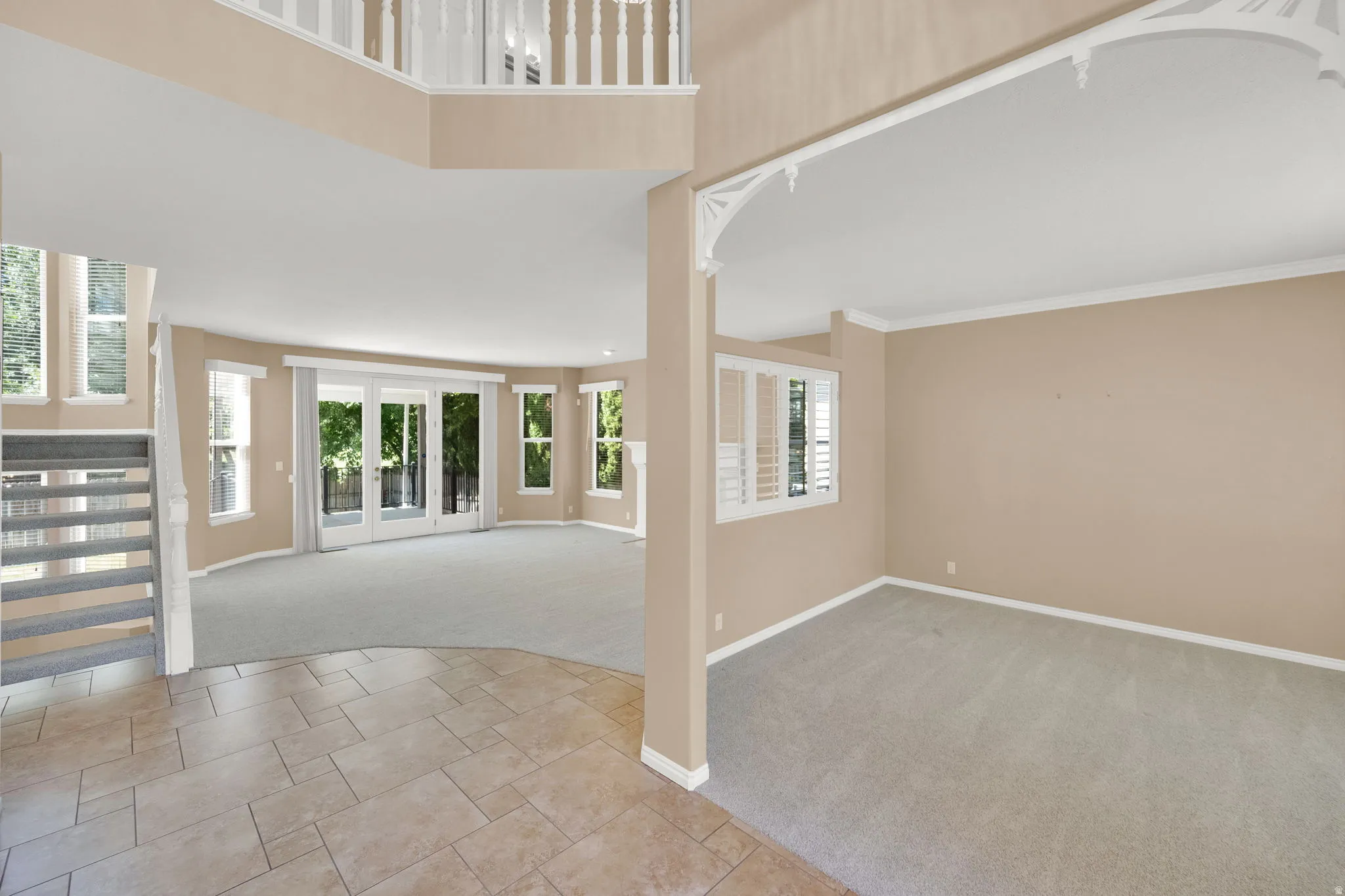 Spacious living area featuring expansive windows, neutral carpeting, and a grand staircase with white balusters