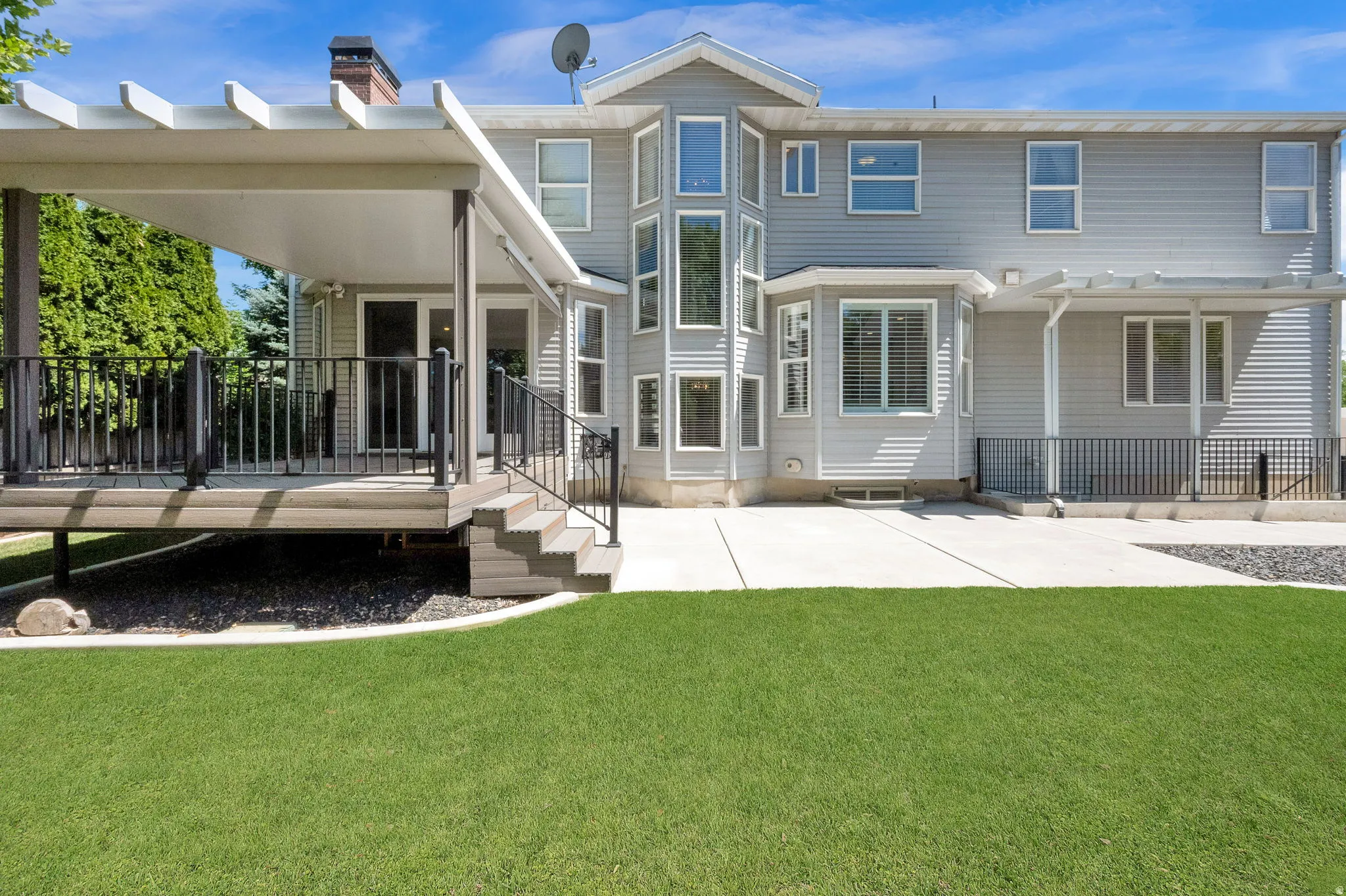 Rear exterior featuring a covered deck with dark railings, a concrete patio, and a manicured lawn