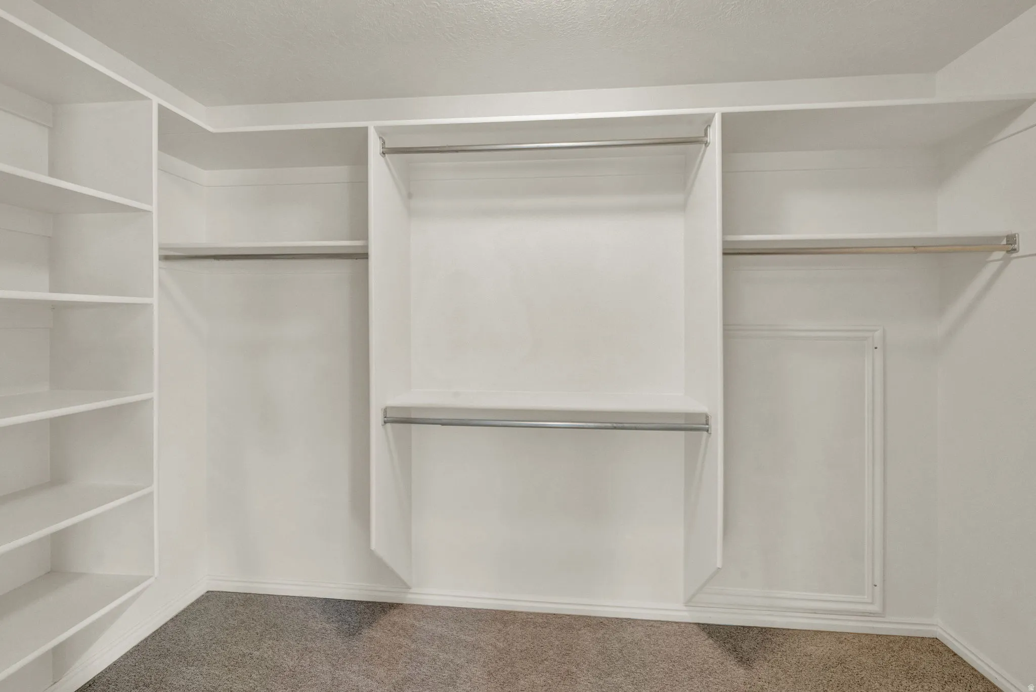 Owners Suite Built-in closet system featuring white shelving, multiple hanging rods, and carpet flooring