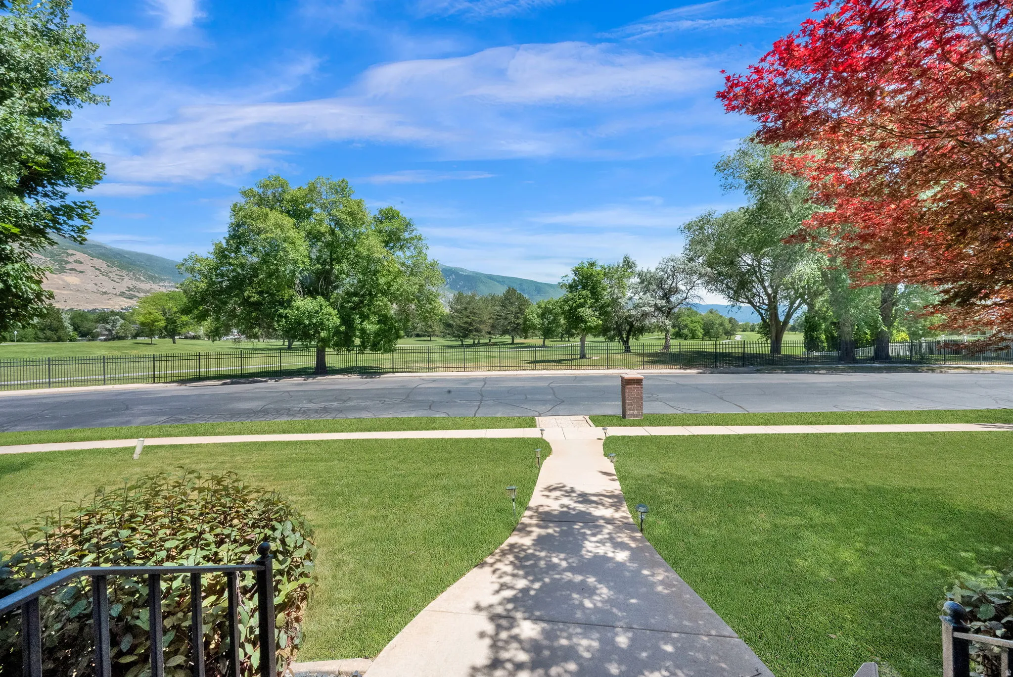 Front yard featuring a concrete walkway, expansive green lawn, and mature landscaping