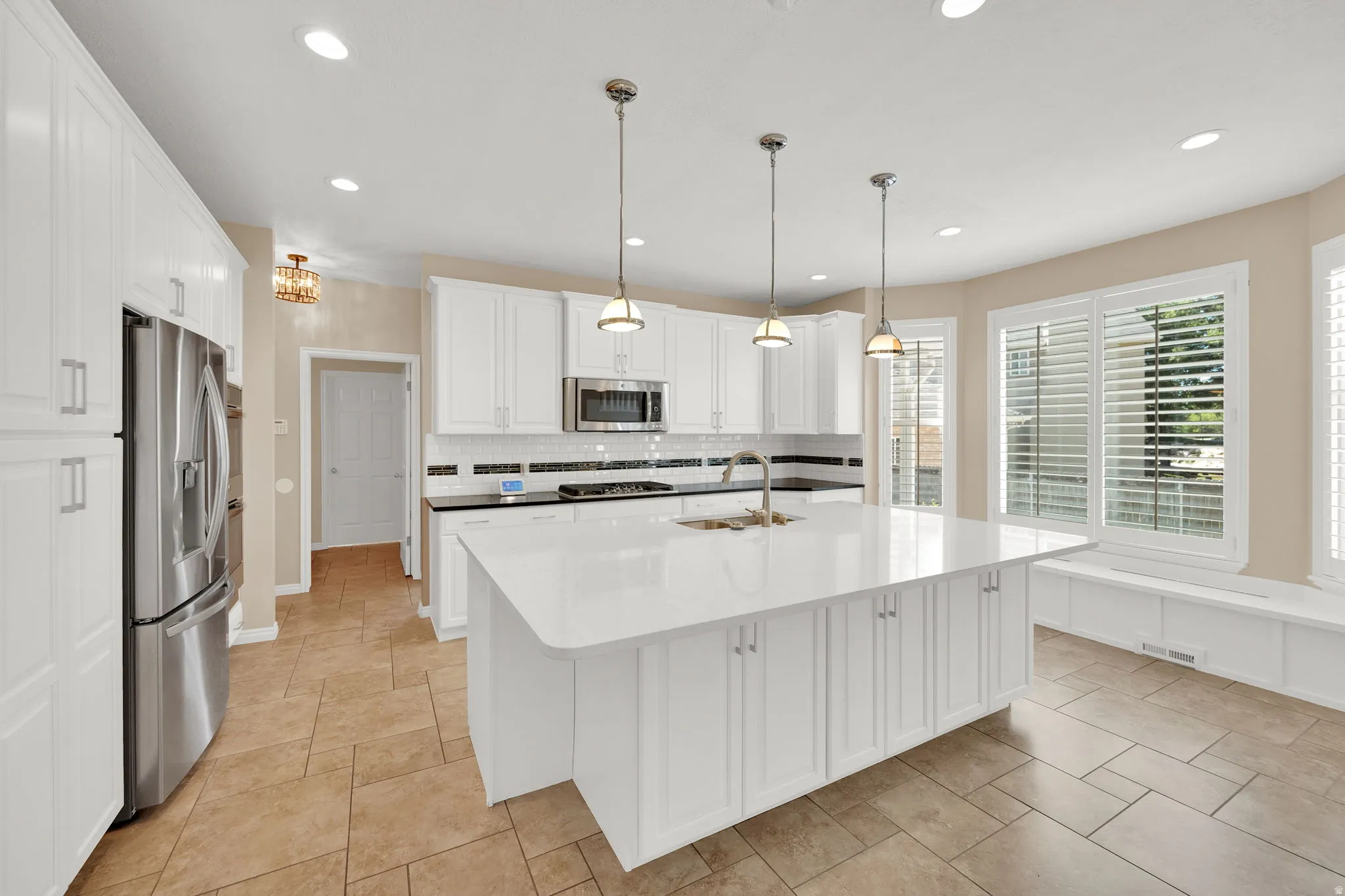 Modern kitchen featuring a large central island with a white countertop, white cabinetry, and stainless steel appliances