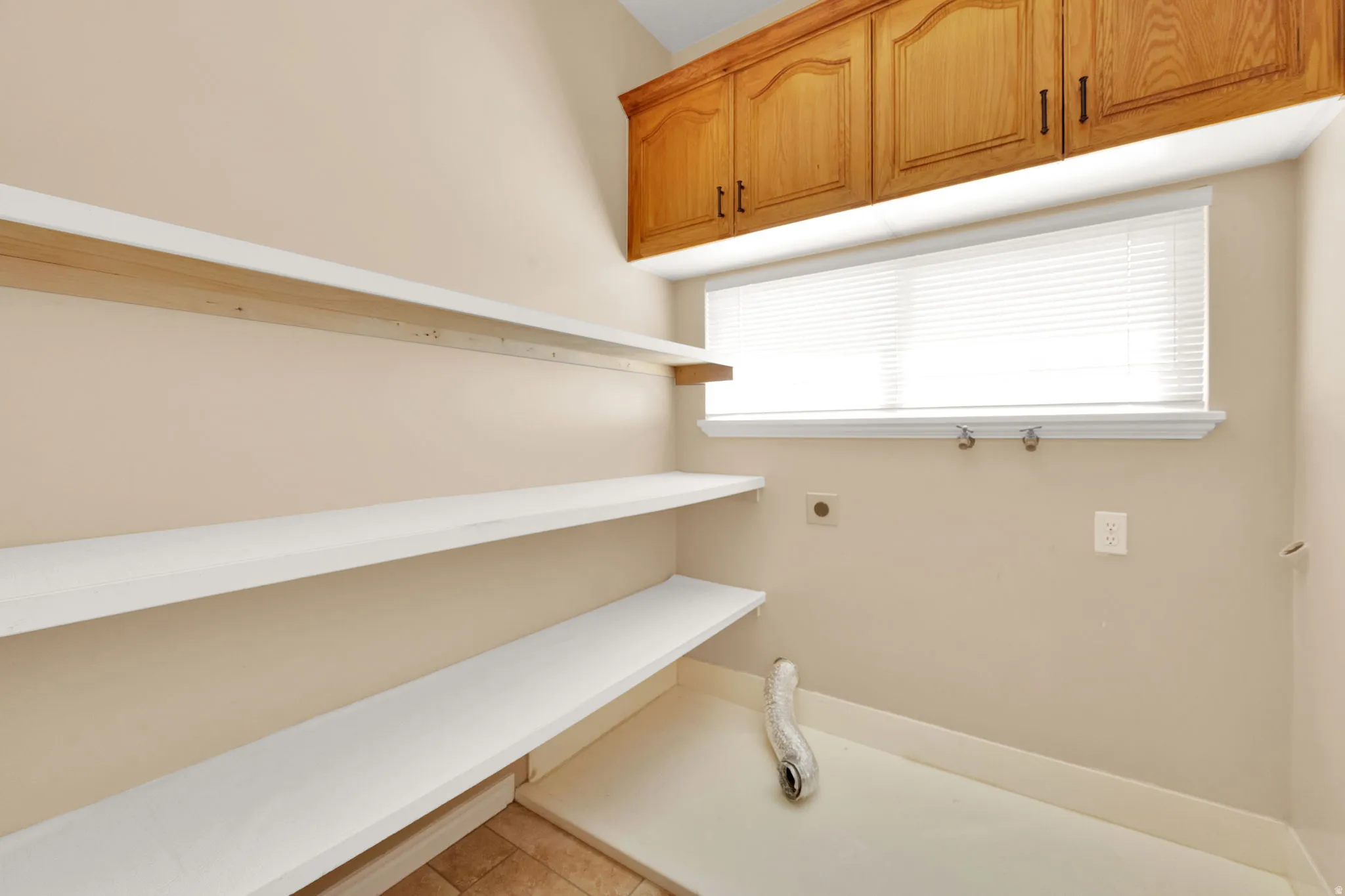 Laundry room featuring built-in shelving, natural wood upper cabinetry, a bright window with blinds, and tile flooring
