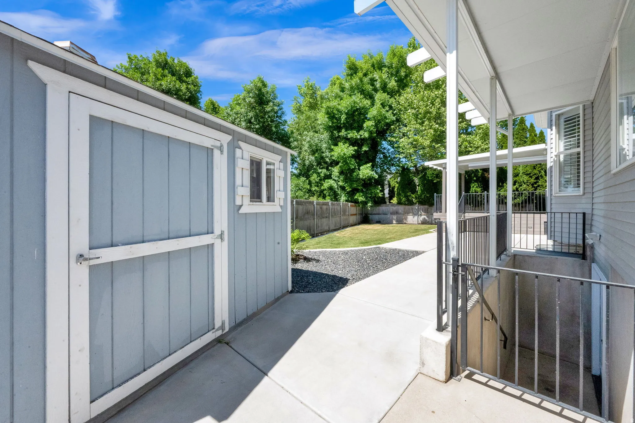 Detached storage shed with a window and white trim, concrete pathway, fenced backyard with lawn, , and exterior entry to lower level