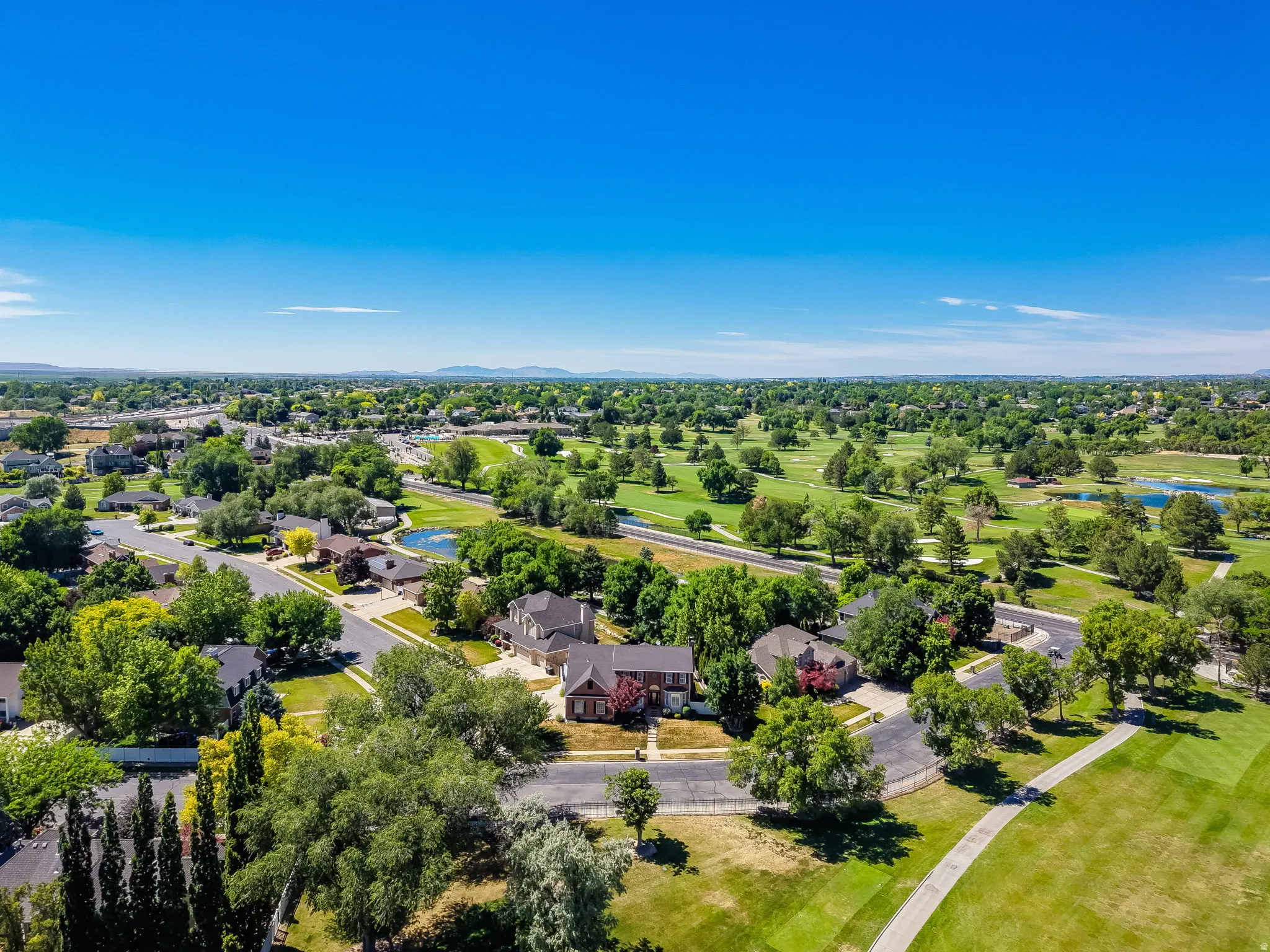 Expansive golf course and residential area featuring mature trees, manicured greens, and a clear blue sky backdrop