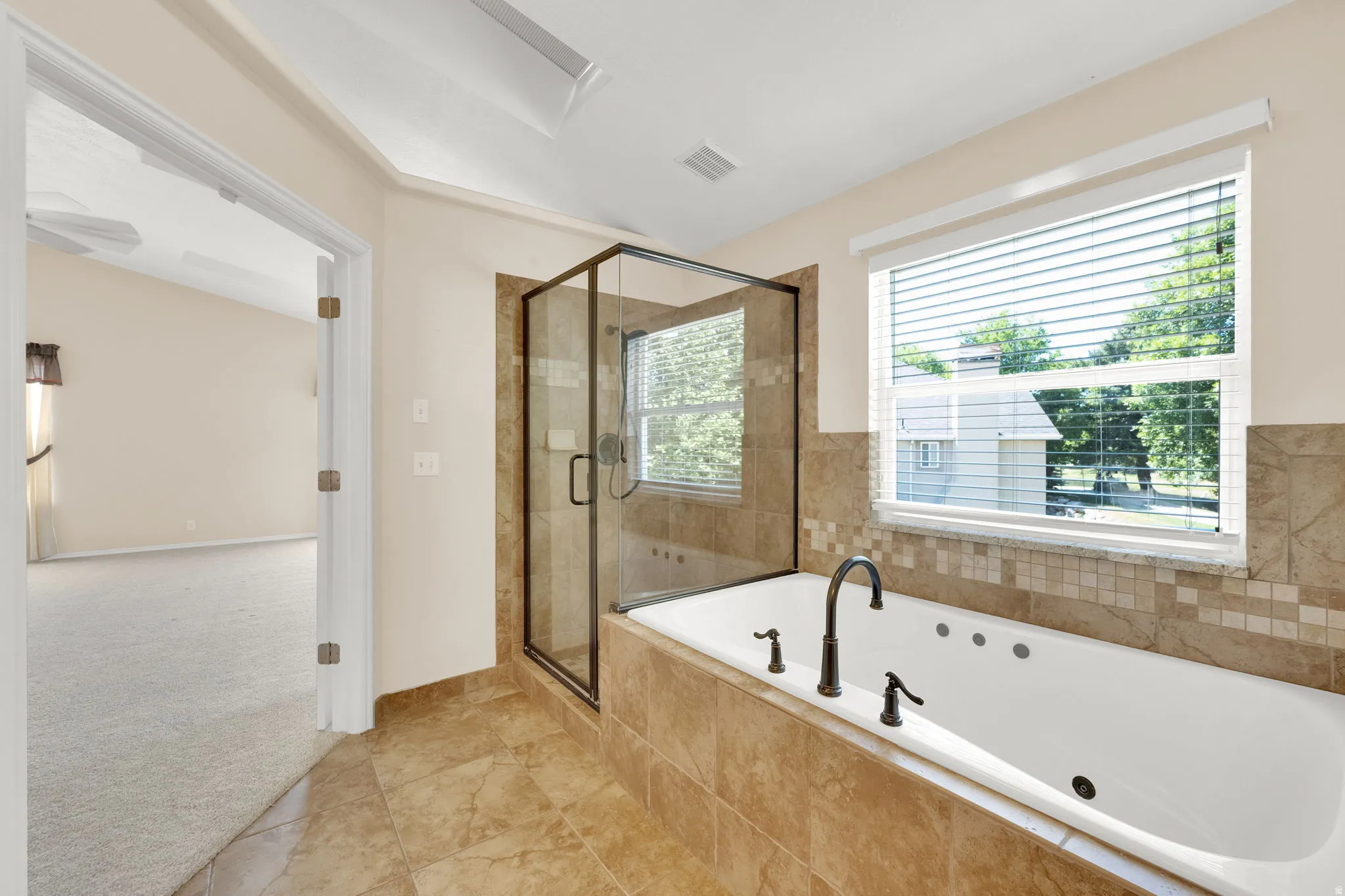 Bathroom featuring a jetted soaking tub with a dark bronze faucet, a glass-enclosed shower, and tiled flooring