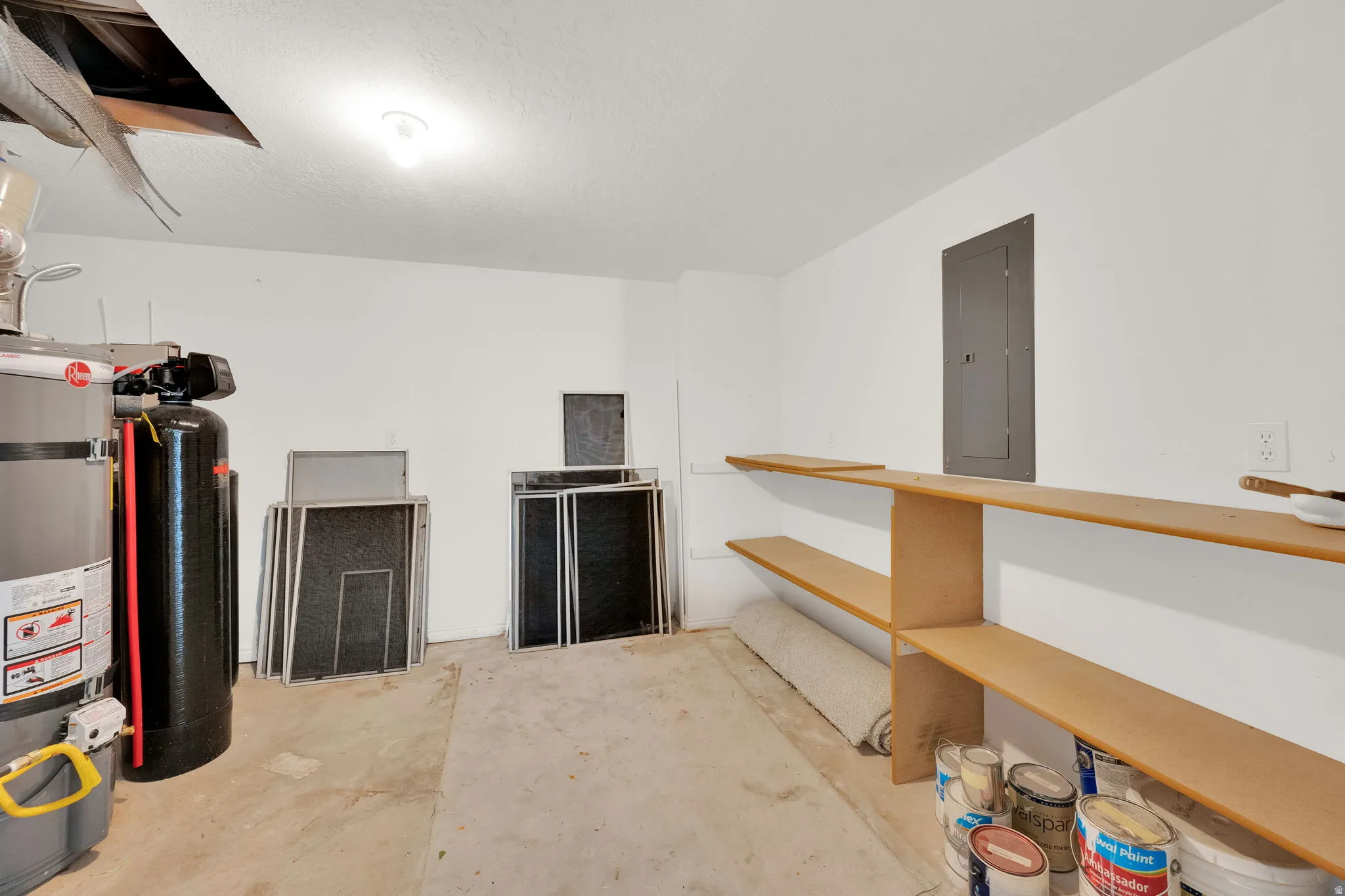 Utility space featuring a water heater, water treatment system, built-in shelving, and a wall-mounted electrical panel