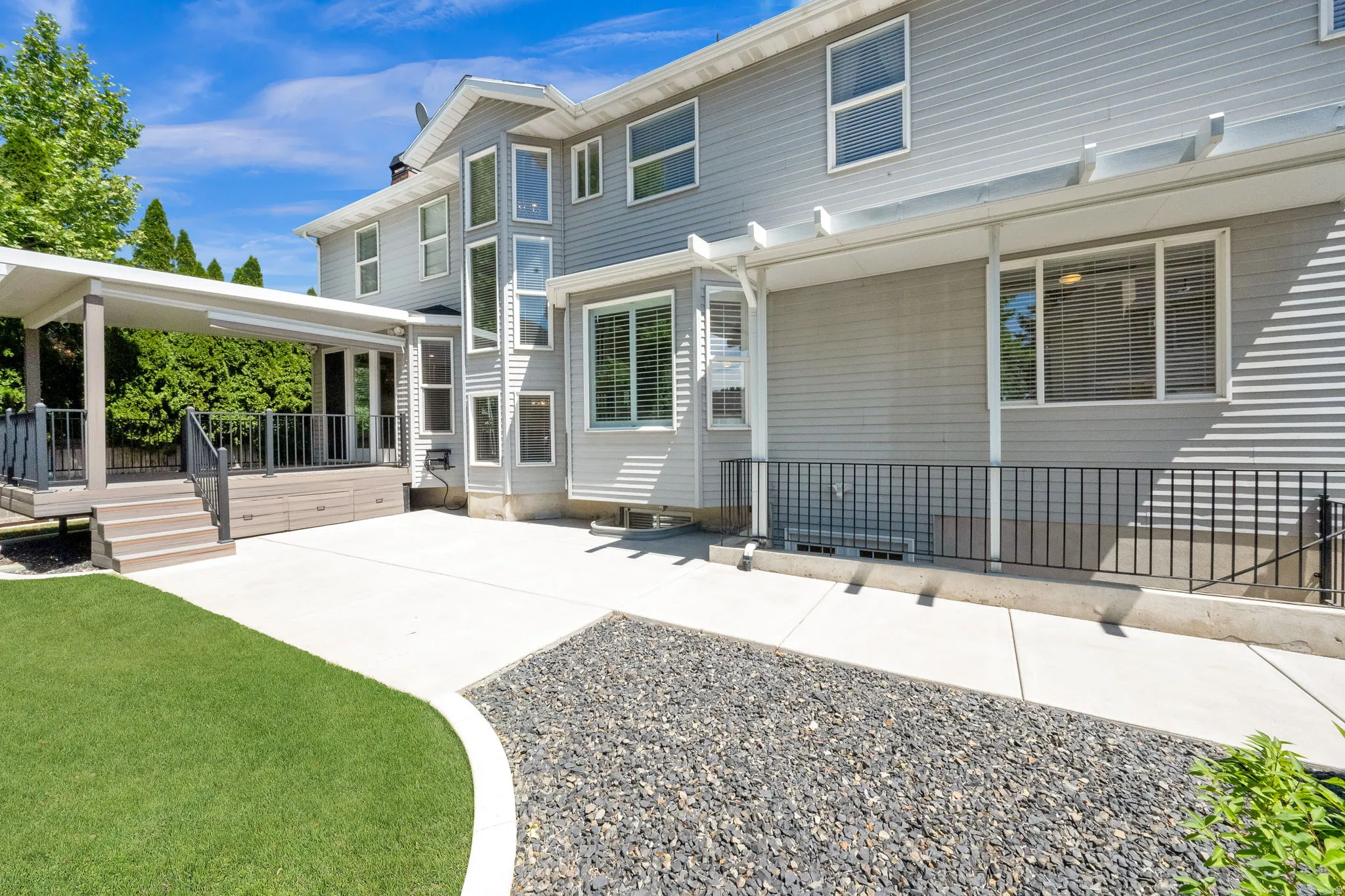 Spacious rear exterior featuring a covered deck, extensive concrete patio, and a decorative gravel bed