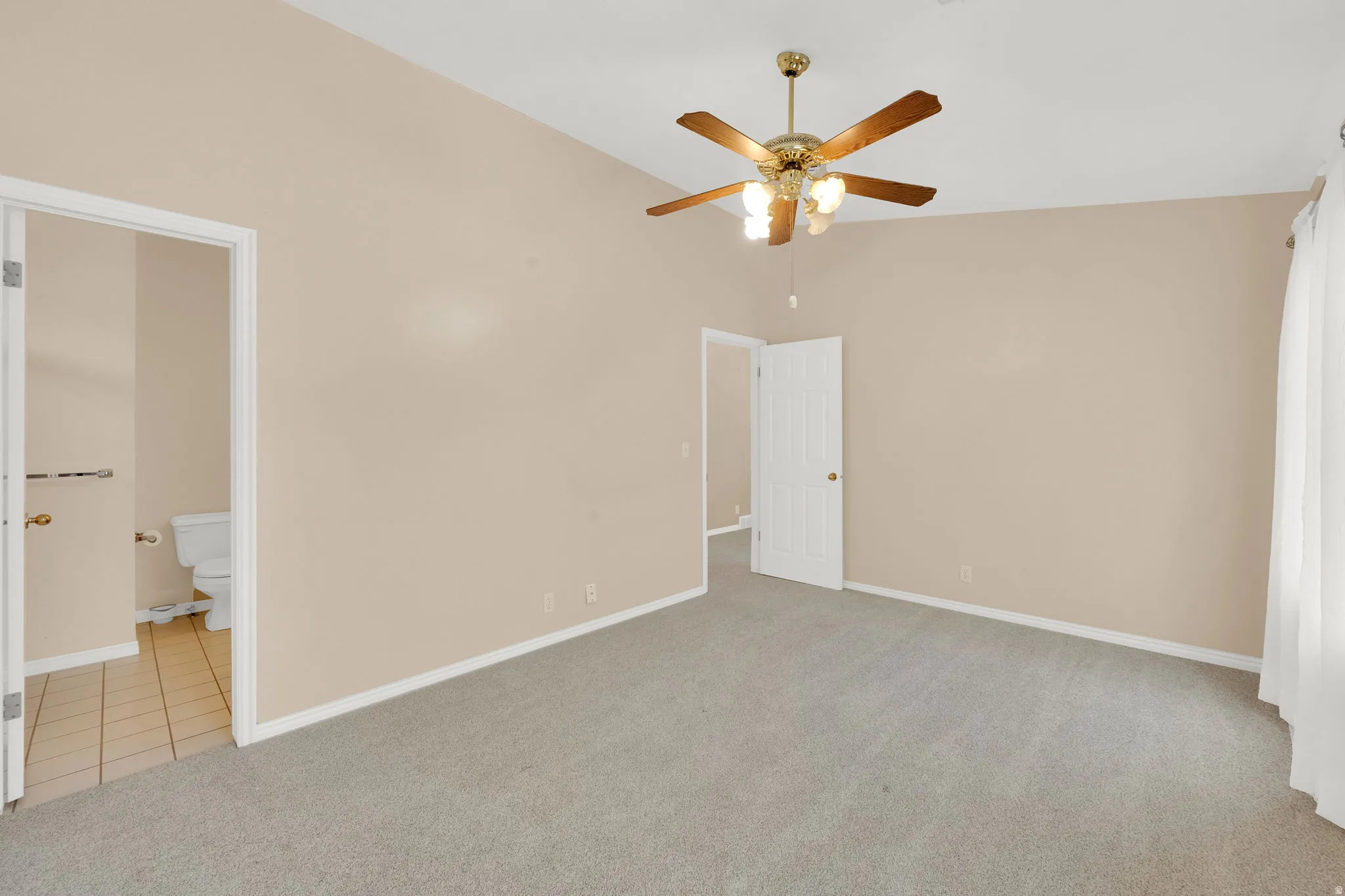 Spacious room featuring vaulted ceilings, a ceiling fan with integrated lighting, neutral-toned walls, and soft grey carpeting