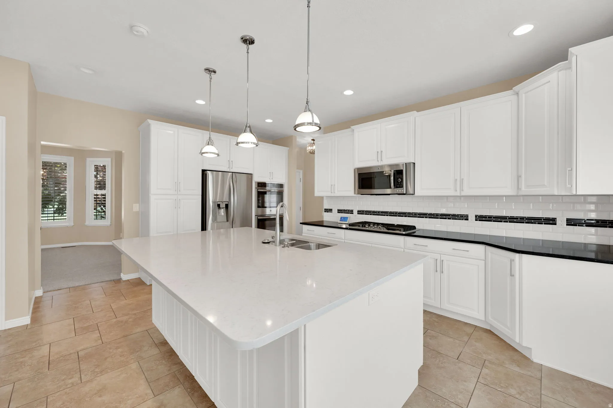 Kitchen featuring an expansive center island with an integrated sink, white cabinetry, and stainless-steel appliances