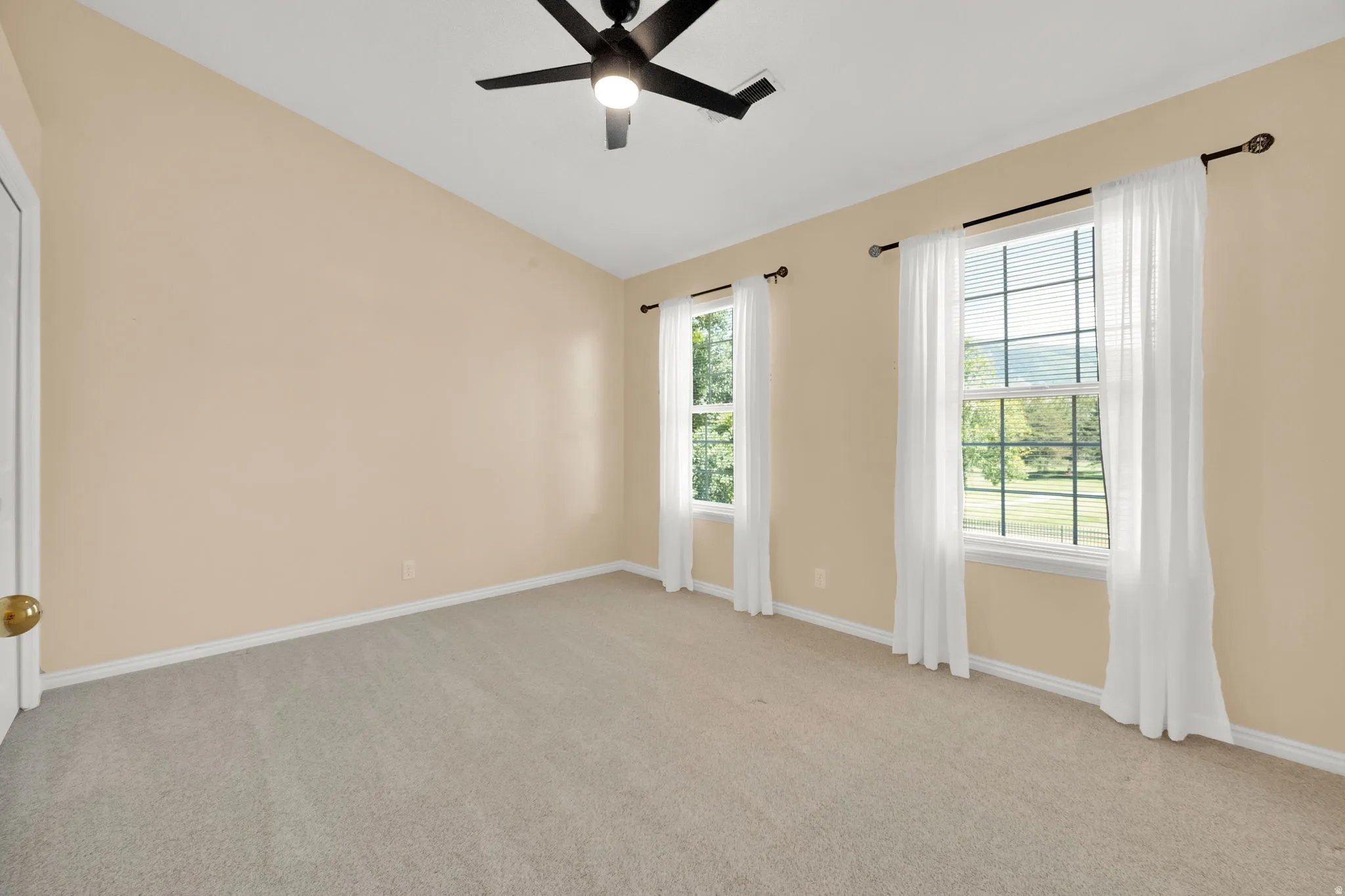 Room featuring a vaulted ceiling with a flush-mount ceiling fan, two double-hung windows, and light-toned carpeting
