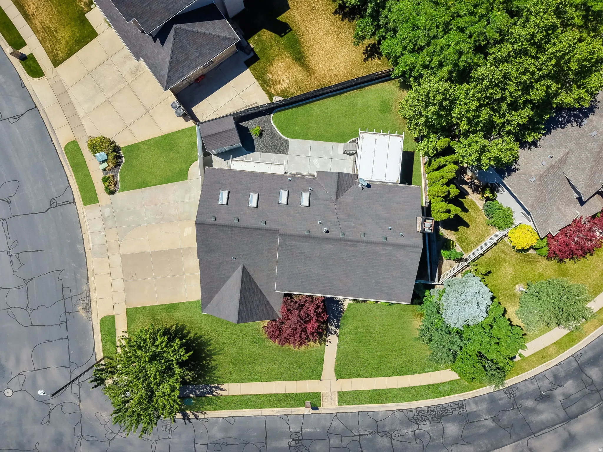 Aerial perspective showcasing a property with a dark shingle roof, multiple skylights, and a neatly manicured lawn