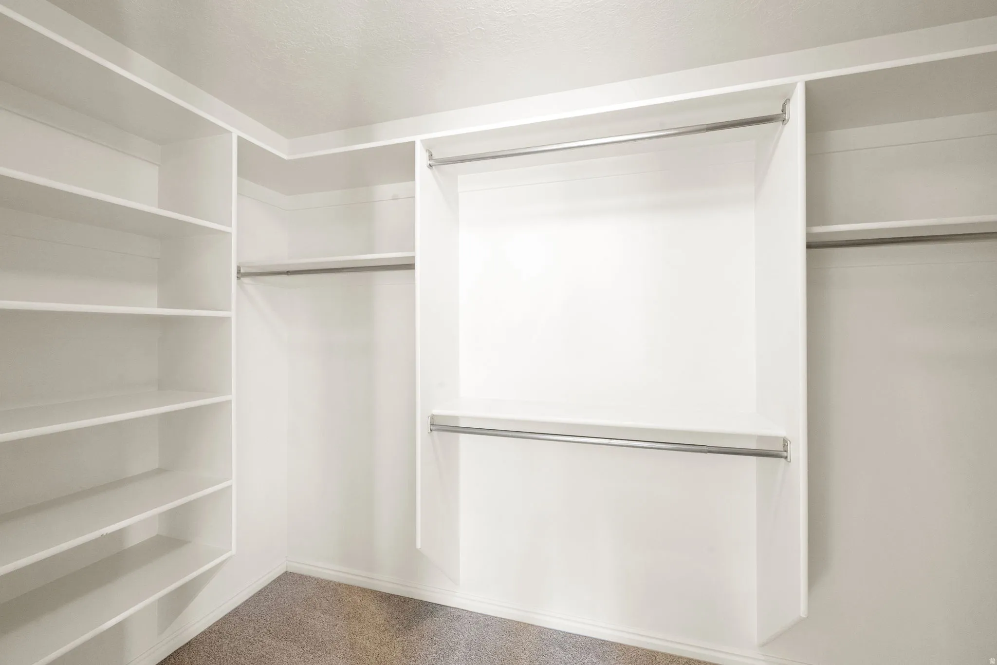 Owners Suite Walk-in closet featuring built-in shelving, multiple hanging rods, and neutral-toned carpeting