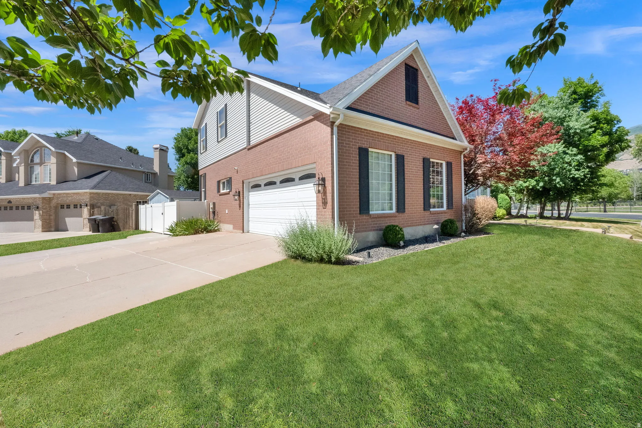 Brick and siding exterior featuring a two-car garage, mature landscaping, and a manicured lawn