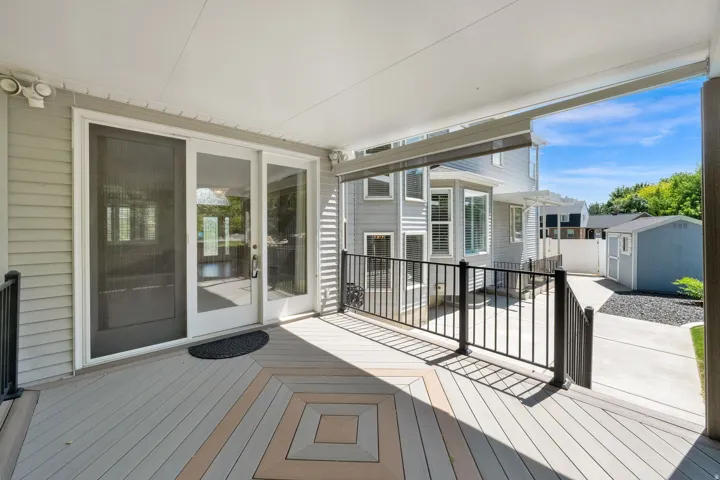 Covered outdoor deck featuring a decorative pattern in the flooring, black metal railings, and a sliding glass door for interior access