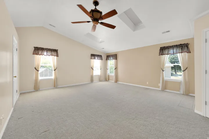 Spacious room featuring vaulted ceilings, a ceiling fan, two skylights, and multiple windows with blinds
