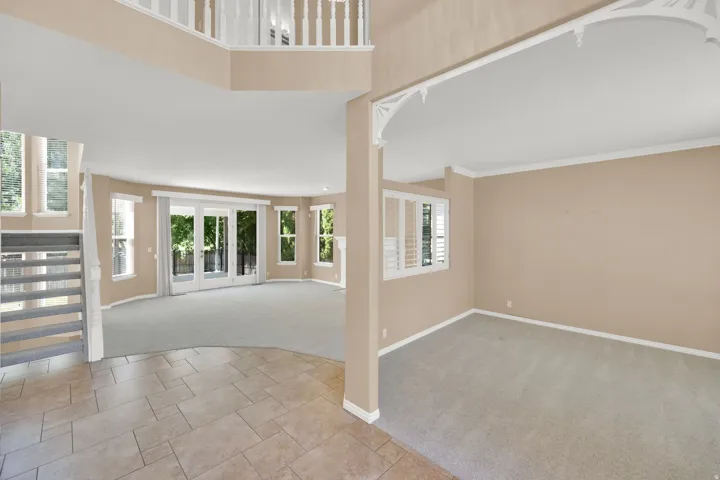 Spacious living area featuring expansive windows, neutral carpeting, and a grand staircase with white balusters
