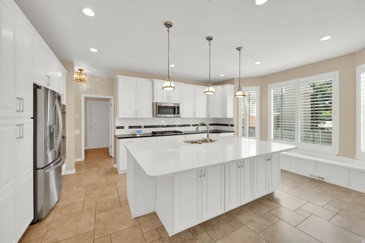 Modern kitchen featuring a large central island with a white countertop, white cabinetry, and stainless steel appliances
