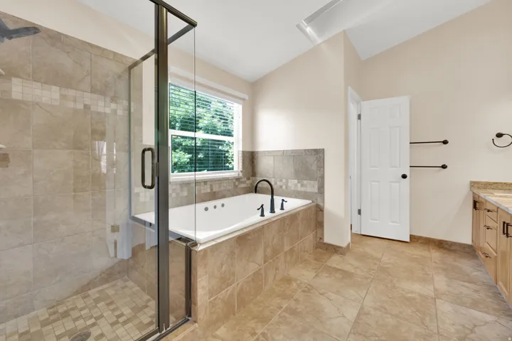 Owners Suite Bathroom Spa-style bathroom featuring a glass-enclosed shower with tile surround, a built-in jetted tub with black