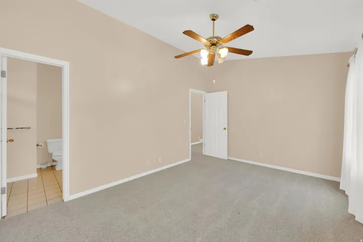 Spacious room featuring vaulted ceilings, a ceiling fan with integrated lighting, neutral-toned walls, and soft grey carpeting