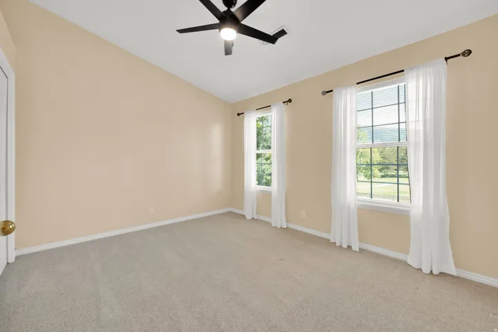 Room featuring a vaulted ceiling with a flush-mount ceiling fan, two double-hung windows, and light-toned carpeting