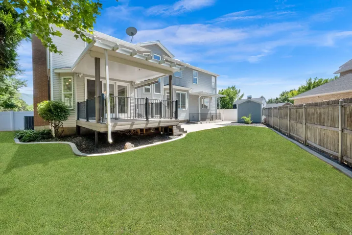 Expansive backyard featuring a manicured lawn, a covered deck with black railings, and a concrete patio