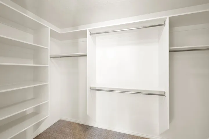 Owners Suite Walk-in closet featuring built-in shelving, multiple hanging rods, and neutral-toned carpeting