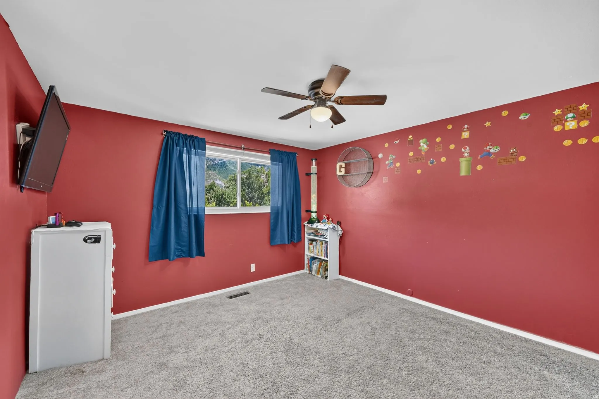 Carpeted room featuring a ceiling fan with integrated lighting, a window showcasing distant hills, and red painted walls