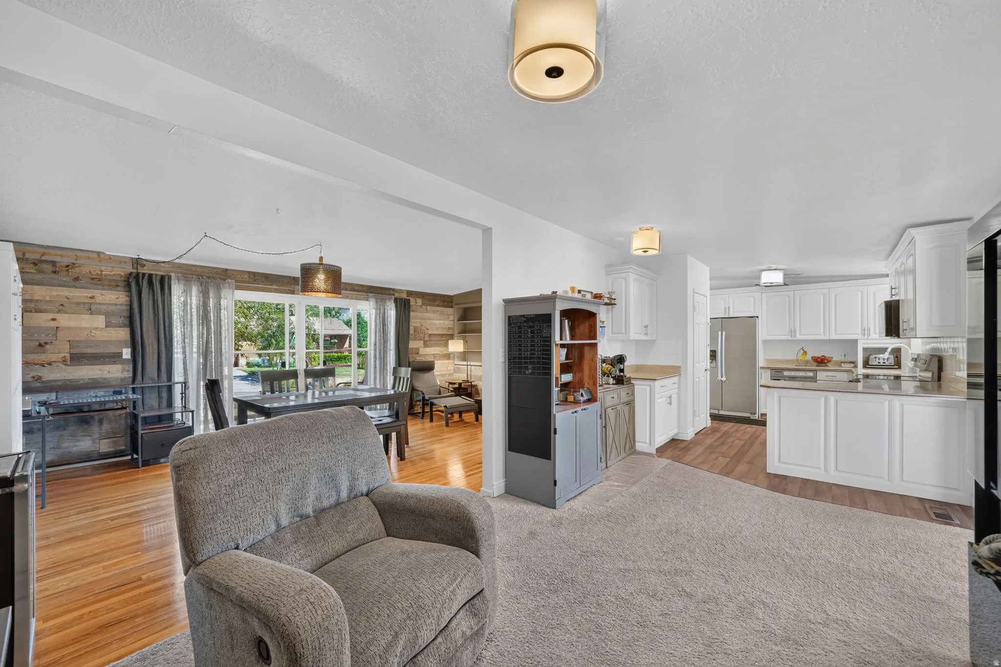Open-concept living space featuring a carpeted area opening to a kitchen with white cabinetry and stainless steel appliances