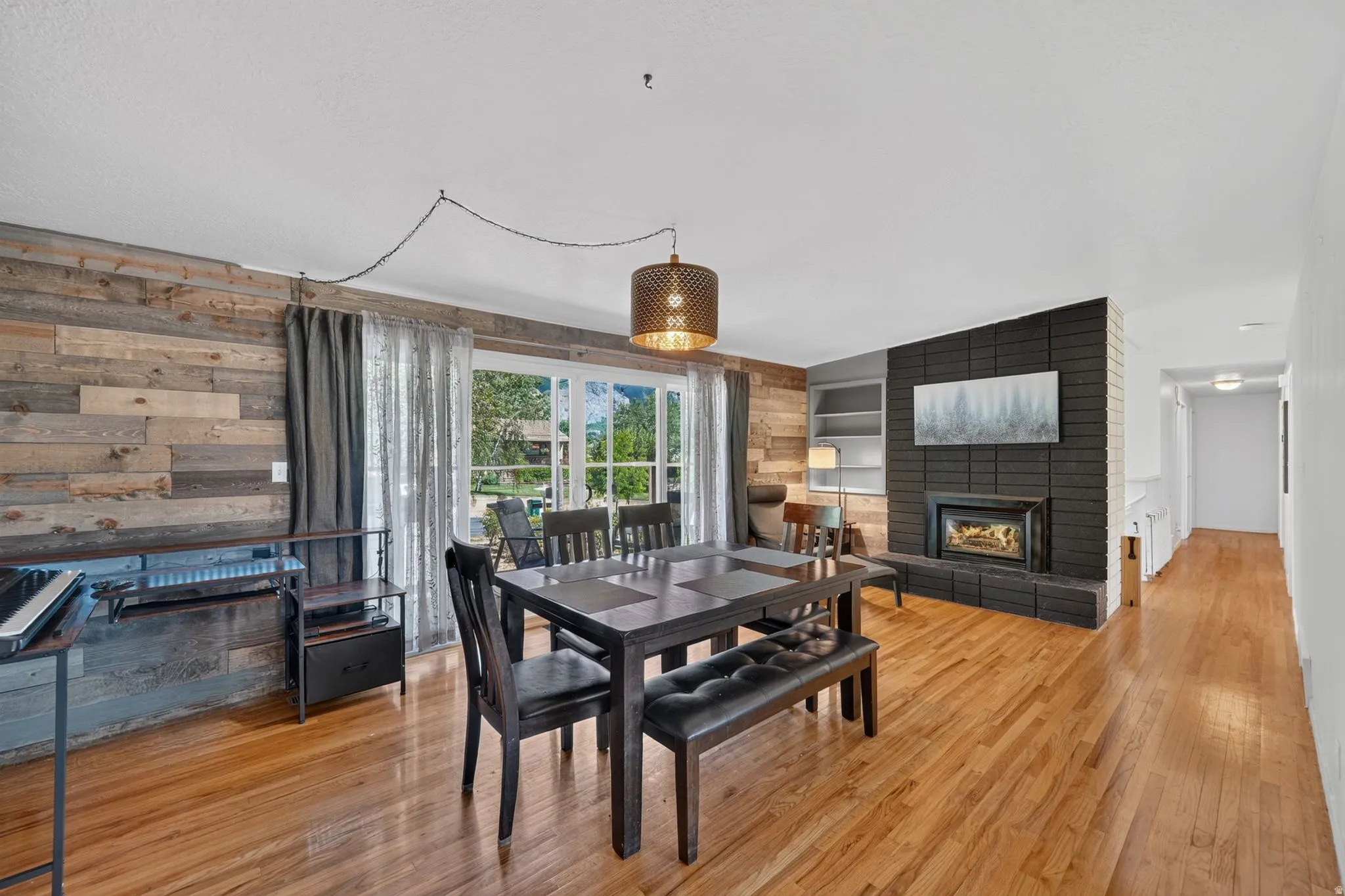 Spacious interior featuring wood-finish flooring, a prominent black brick fireplace, a feature wall with horizontal wood paneling, built-in shelving, and large sliding glass doors providing ample natural light
