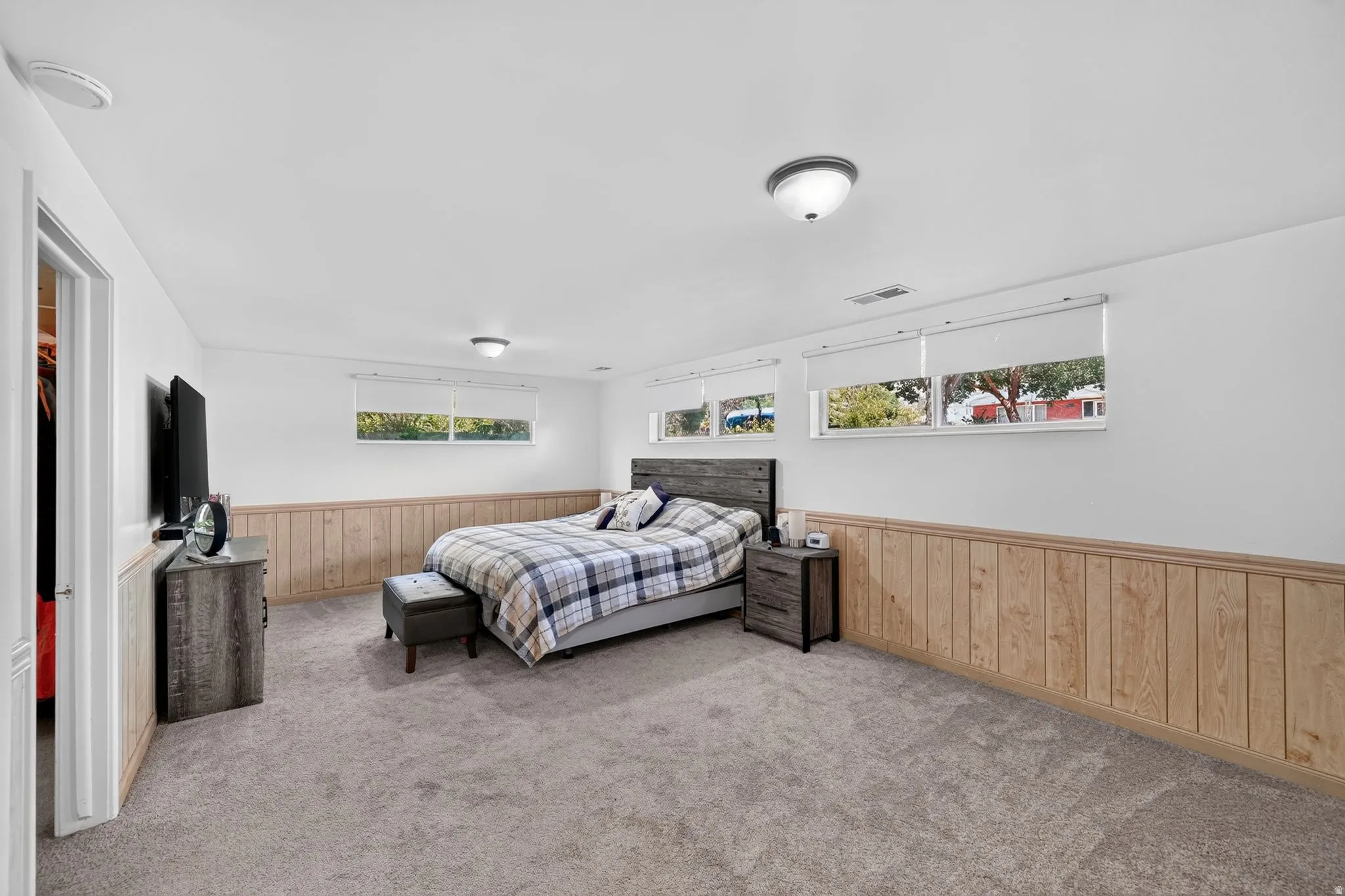 Spacious room featuring light-colored carpeting, white walls, and wood paneling along the lower wall