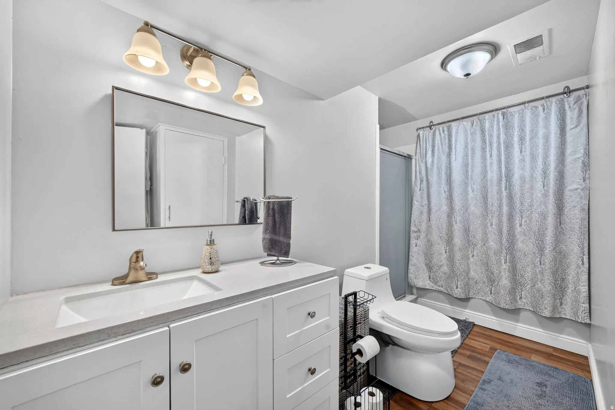Bathroom featuring a white vanity with integrated sink, rectangular mirror, and a three-light fixture