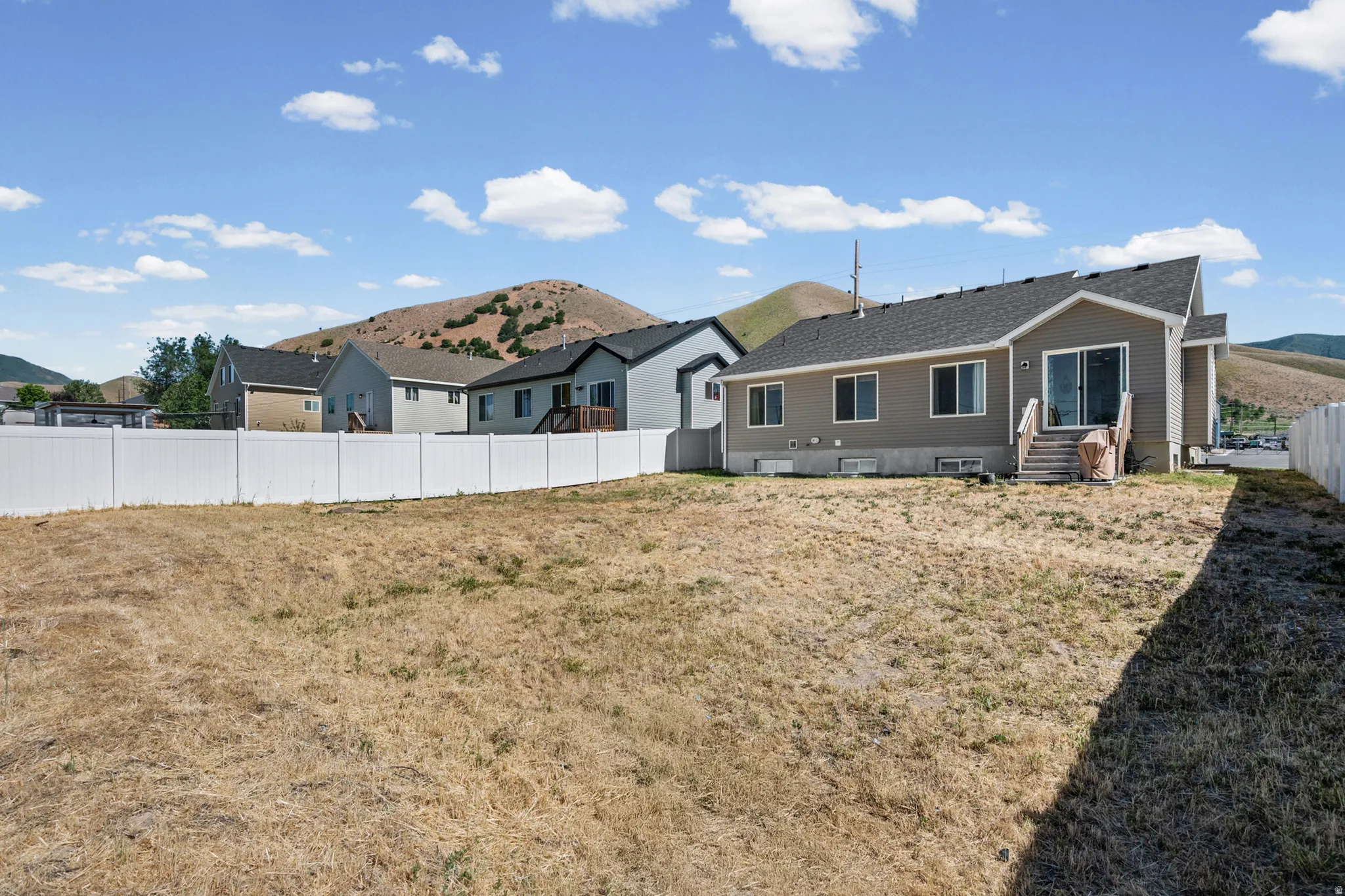 Expansive backyard space featuring a vinyl privacy fence, a partial wood deck, and direct access to the interior via a sliding glass door