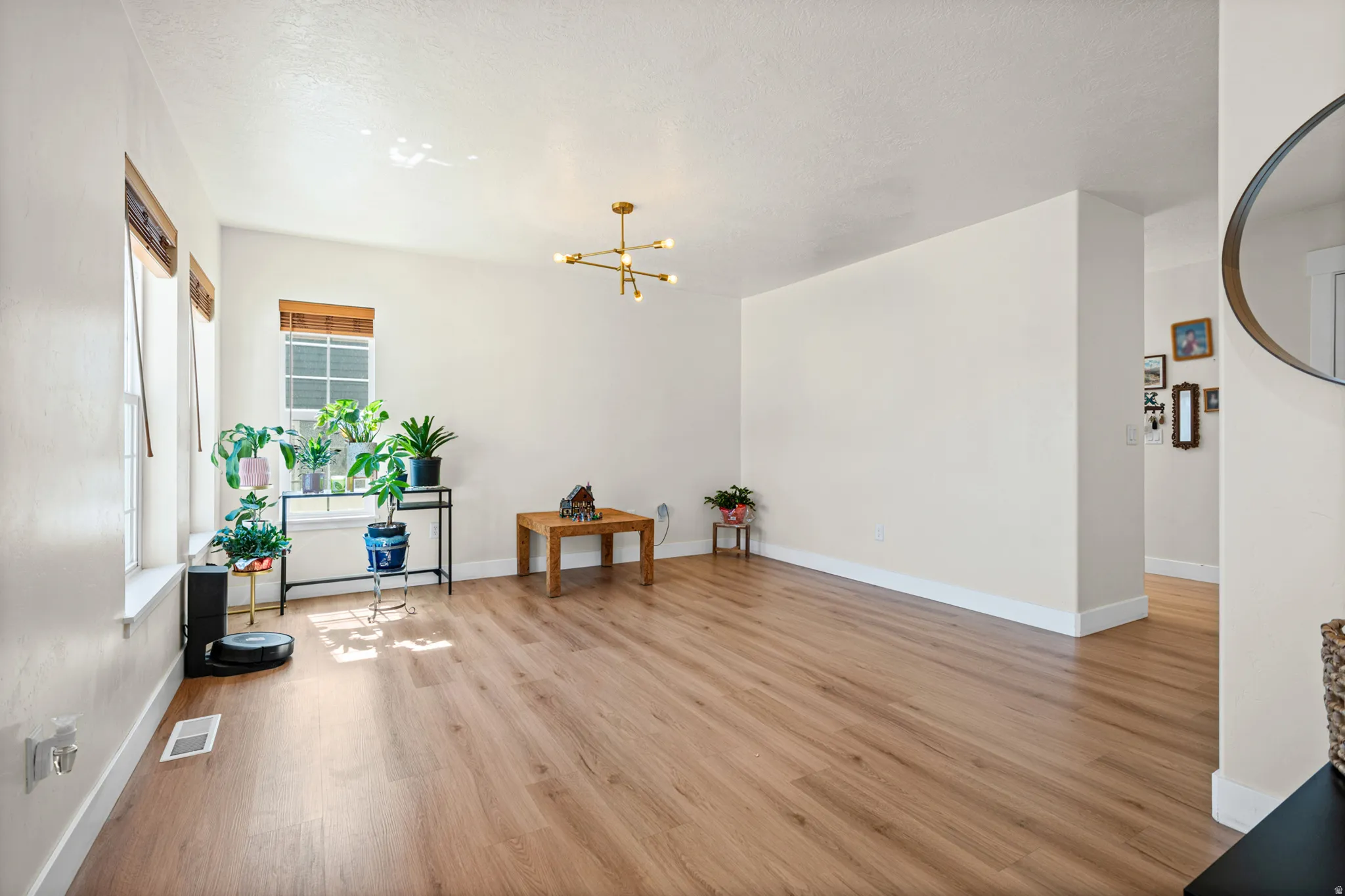 Open-concept living space with wood-finish flooring, multiple windows, and a modern brass chandelier