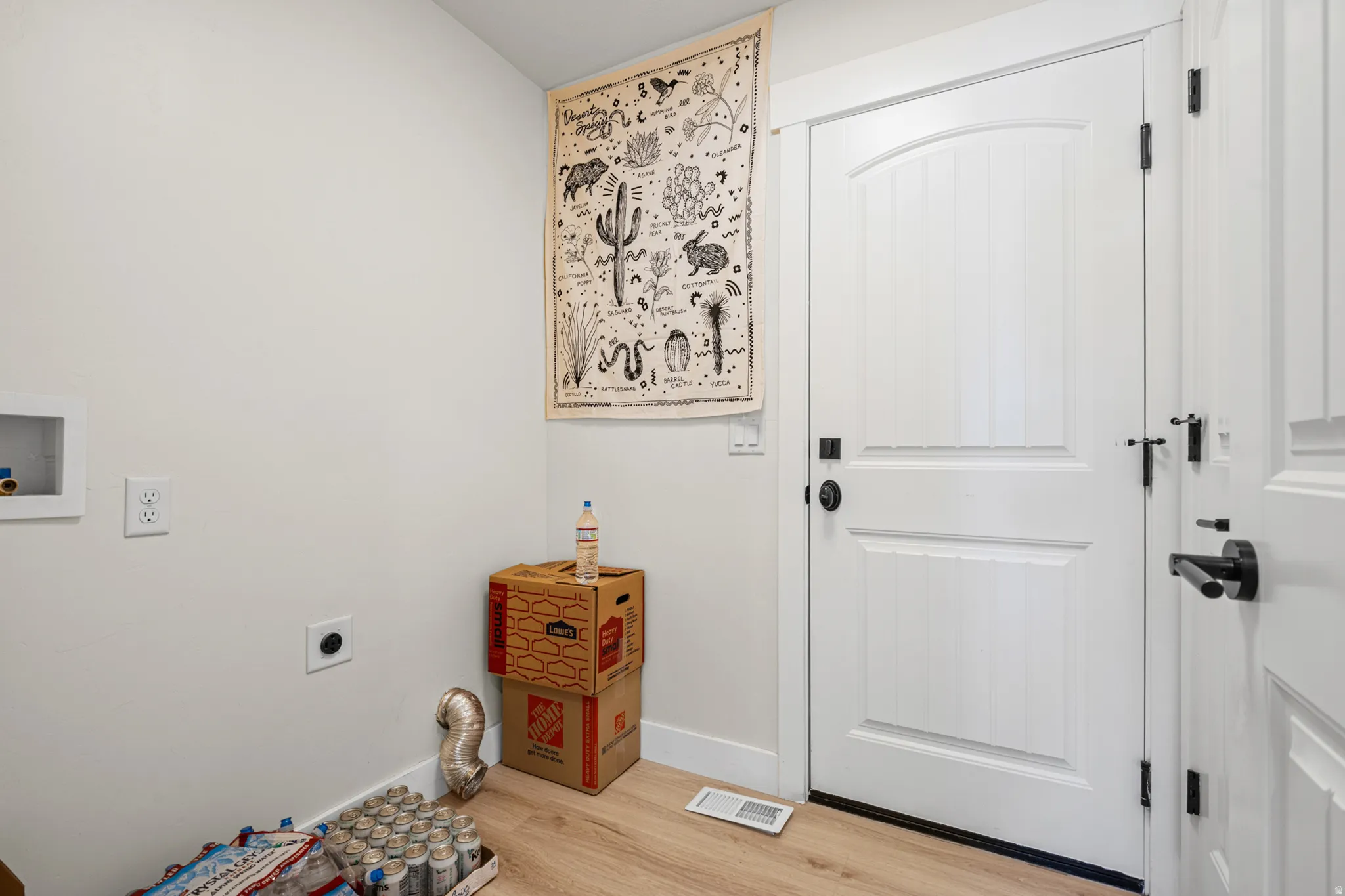 Utility area featuring light wood-finish flooring, white walls, and a white arched panel door with matte black hardware