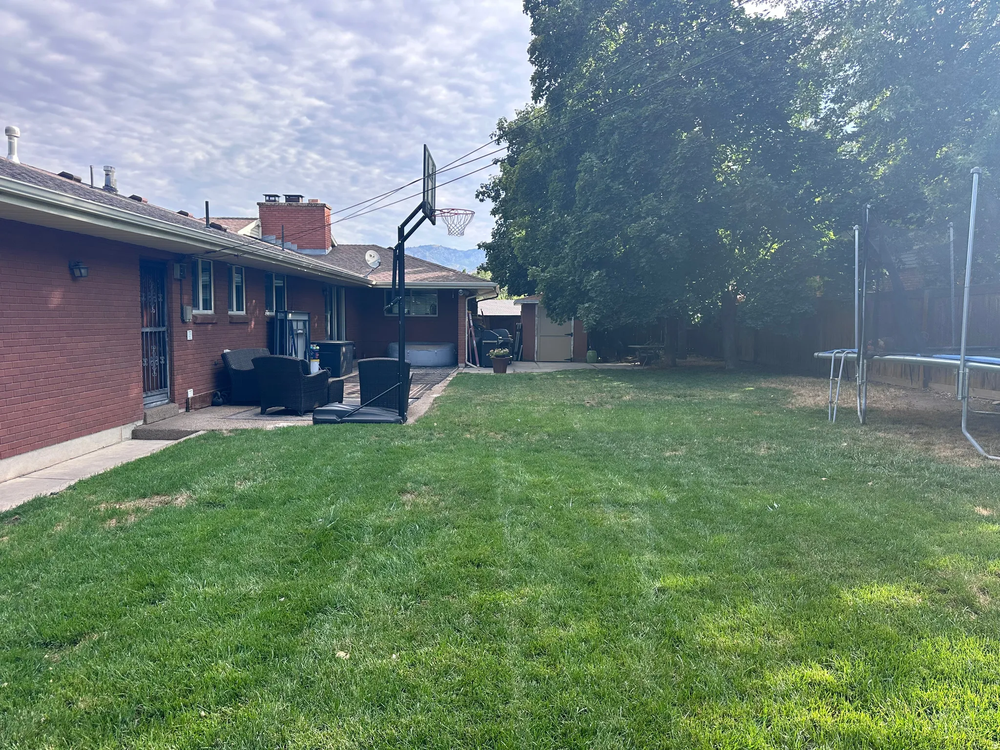 Spacious backyard featuring a large grass area, mature trees, a concrete patio, and a red brick exterior