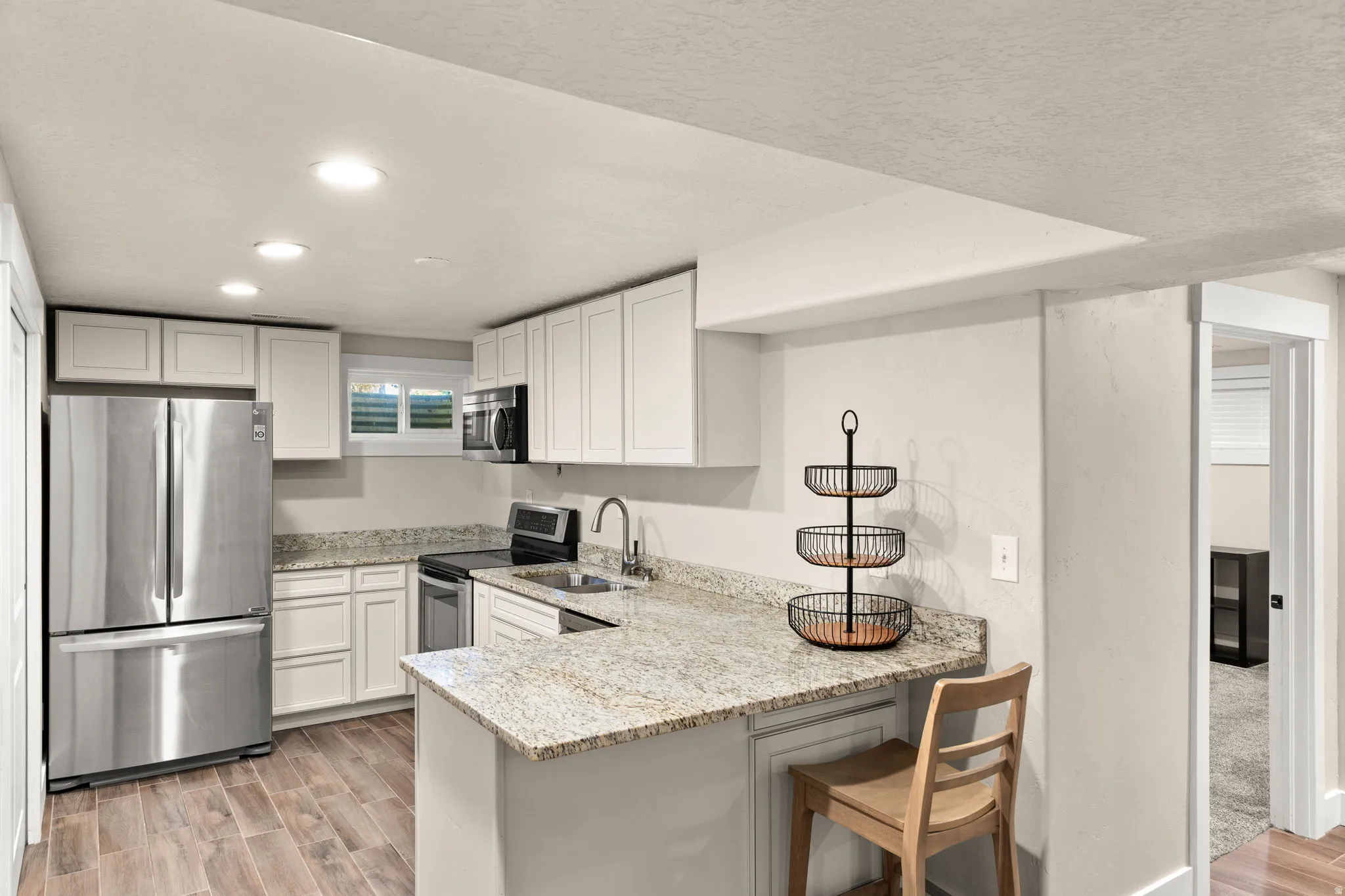 Modern kitchen featuring White cabinetry, Stainless steel appliances, Microwave, Dishwasher, Speckled Stone countertops, and wood-finish flooring!  Large Pantry!