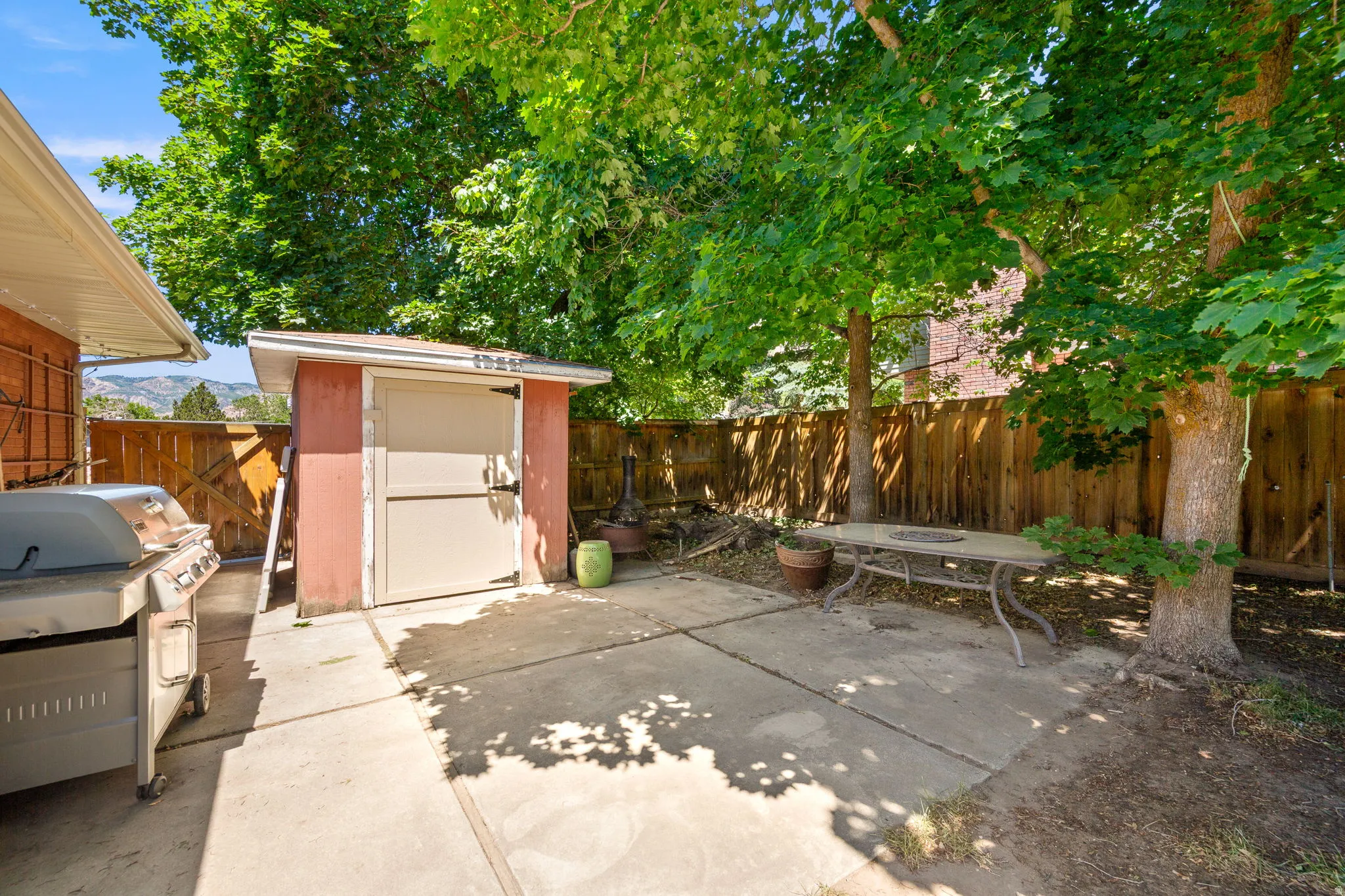 Outdoor patio space with a built-in storage shed, concrete paving, a wood fence perimeter, and mature trees providing natural canopy!