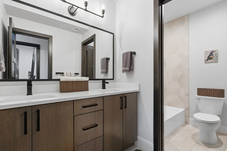 Modern bathroom featuring a dual vanity with wood-finish cabinetry and black hardware